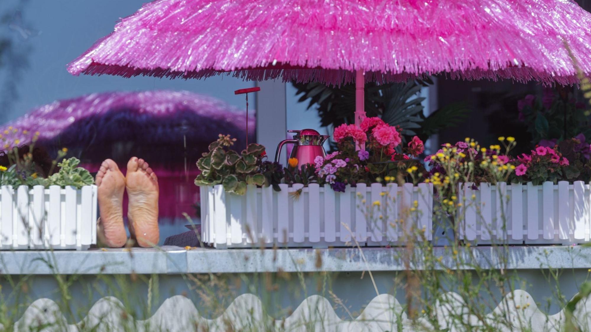 Frau liegt auf einem Balkon unter einem pinken Sonnenschirm