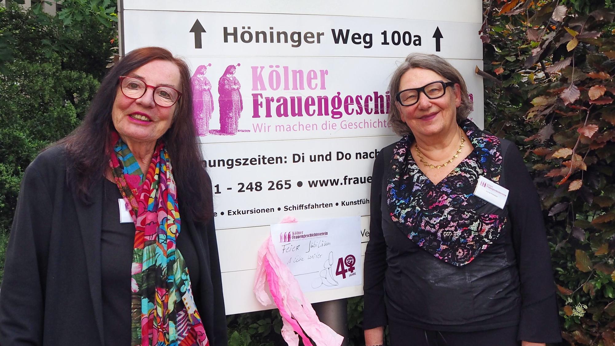 Zwei Frauen in festlicher Kleidung stehen neben dem Schild, das auf die Adresse des Kölner Frauengeschichtsvereins weist.