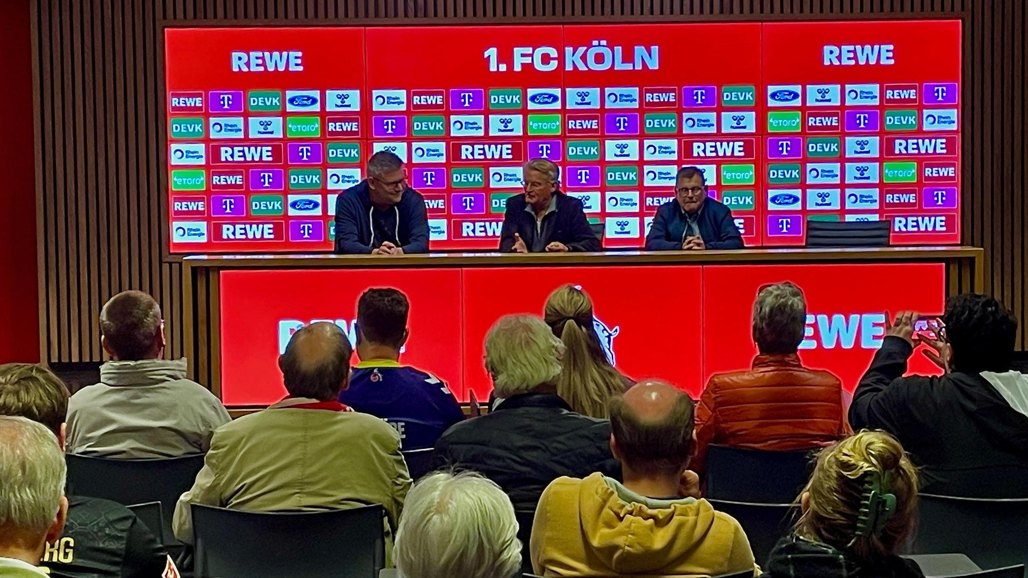 Menschen sitzen auf Stühlen und schauen auf das Set-up der FC-Pressekonferenz. Dort sitzt in der Mitte Michael Trippel.