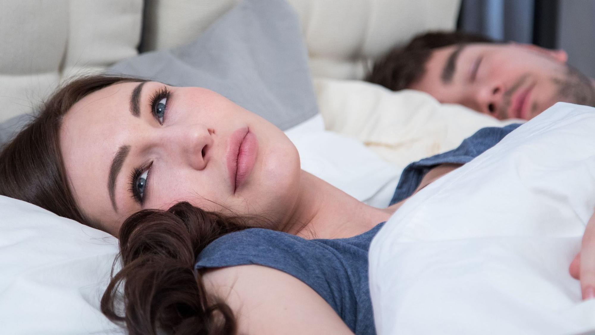 Eine junge Frau liegt wach neben ihrem Partner im Bett
