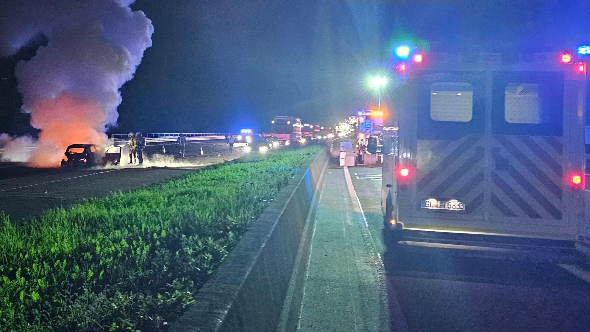 Feuerwehrleute löschen auf einer Autobahn ein in Flammen stehendes Auto.