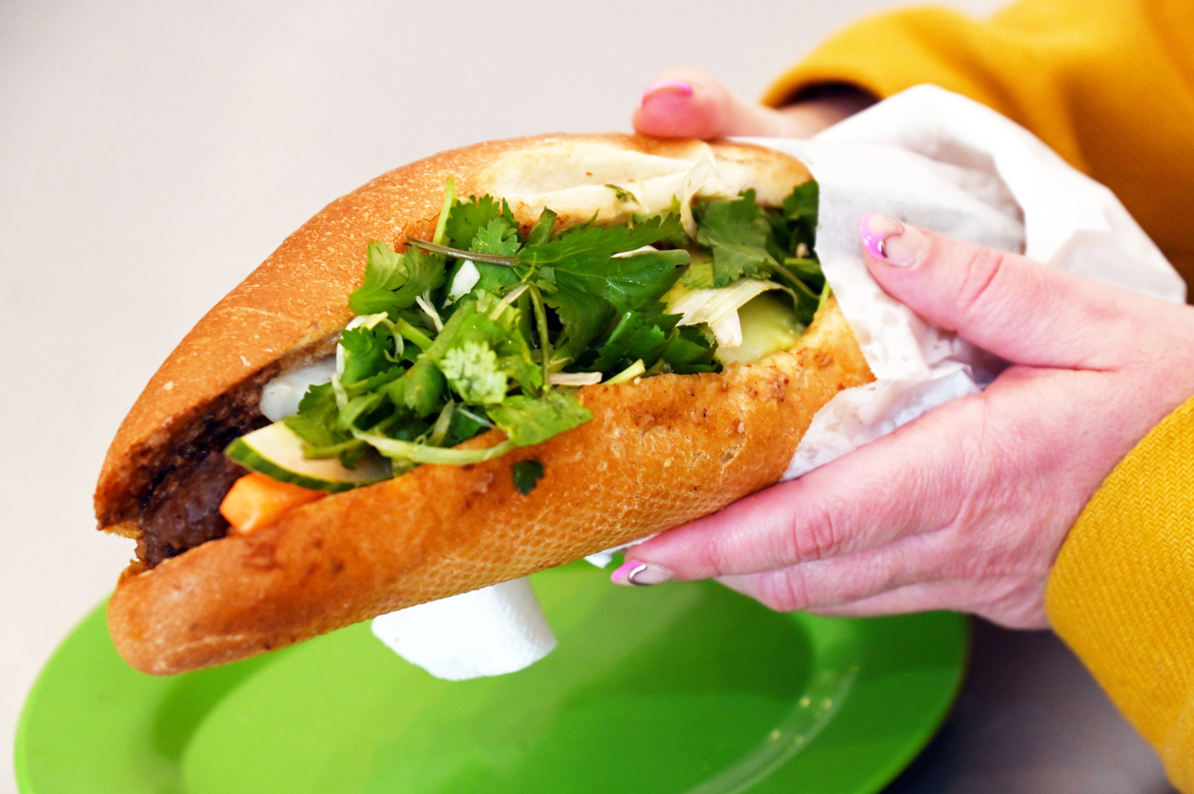 Ein dckes Sandwich mit Salat wird von einer Hand in die Kamera gehalten.