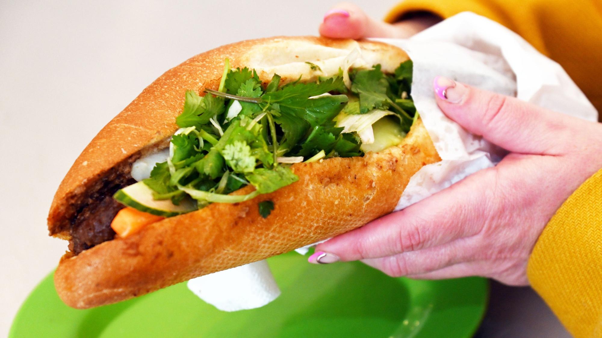 Ein dckes Sandwich mit Salat wird von einer Hand in die Kamera gehalten.
