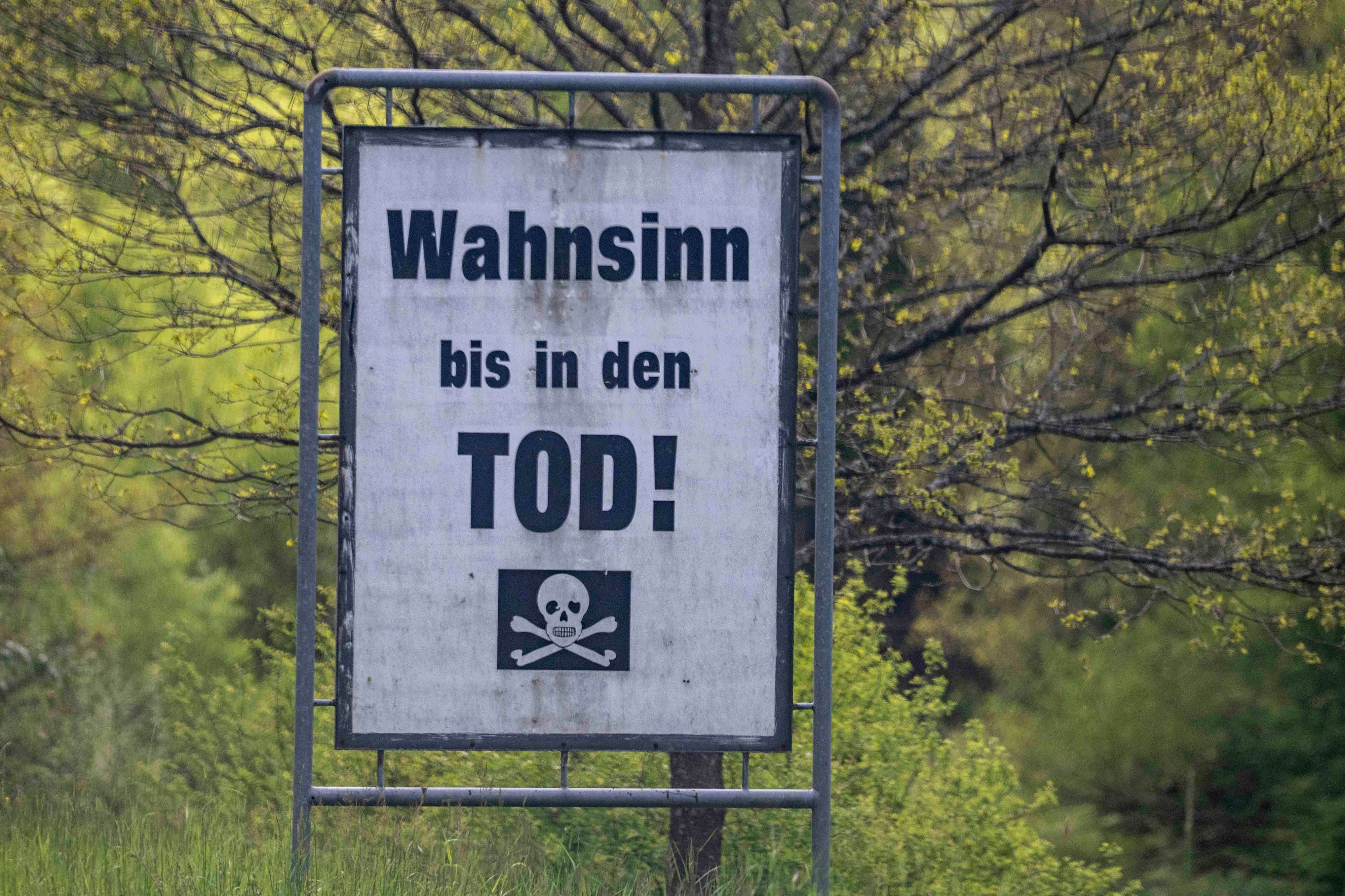 Das Bild zeigt eine Warntafel an einer Straße in der Eifel. „Wahnsinn bis in den Tod“ ist darauf zu lesen.
