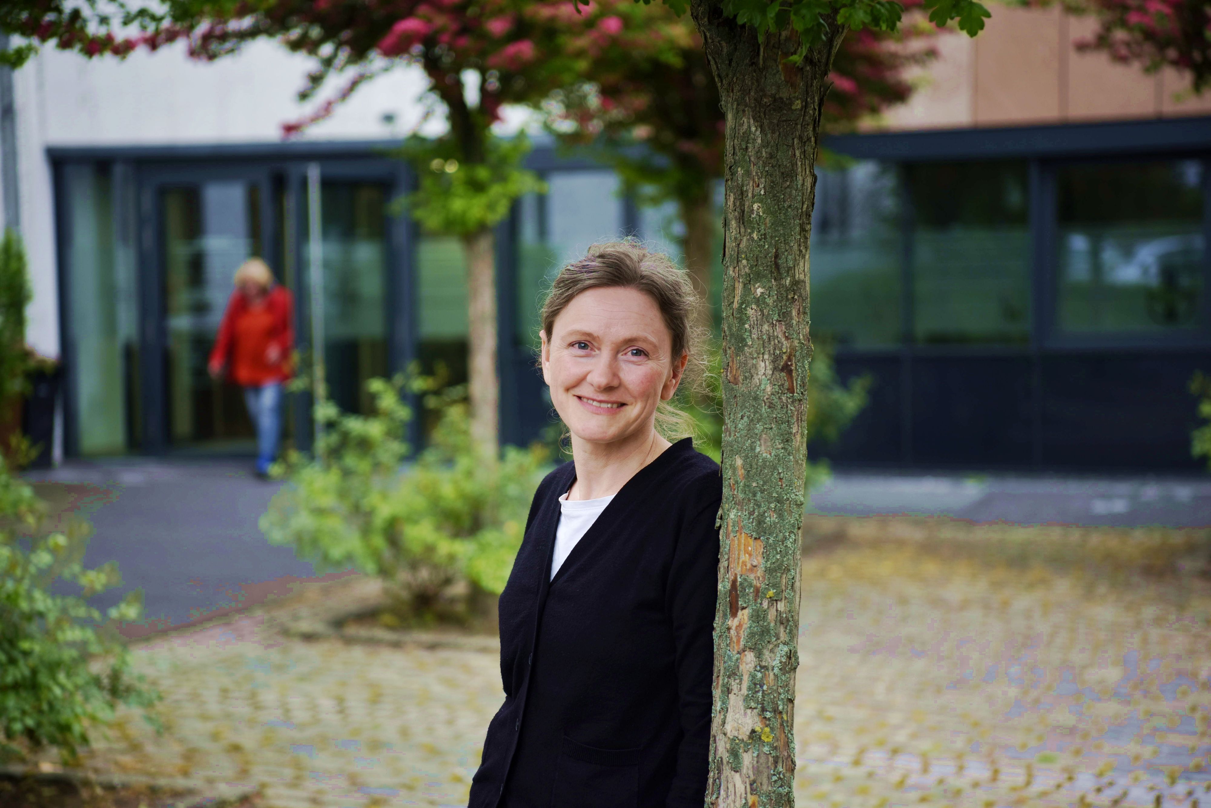 Klimaschutzmanagerin Beatrix Brömme lehnt an einem Baum im Rathausinnenhof. Sie trägt einen schwarzen Pullover.