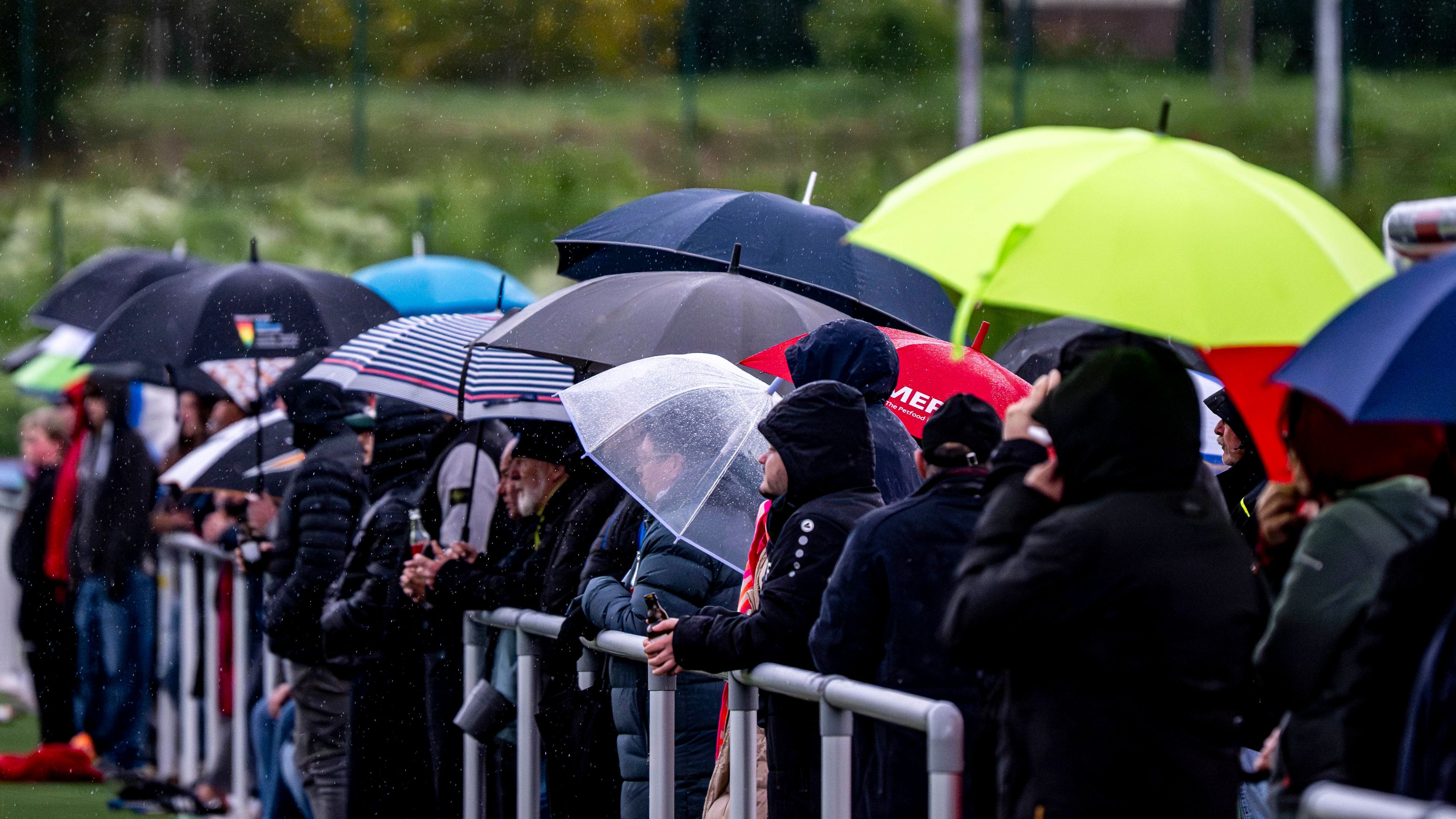Das Bild zeigt zahlreiche Zuschauer, die sich mithilfe von Regenschirmen vor Regen schützen.