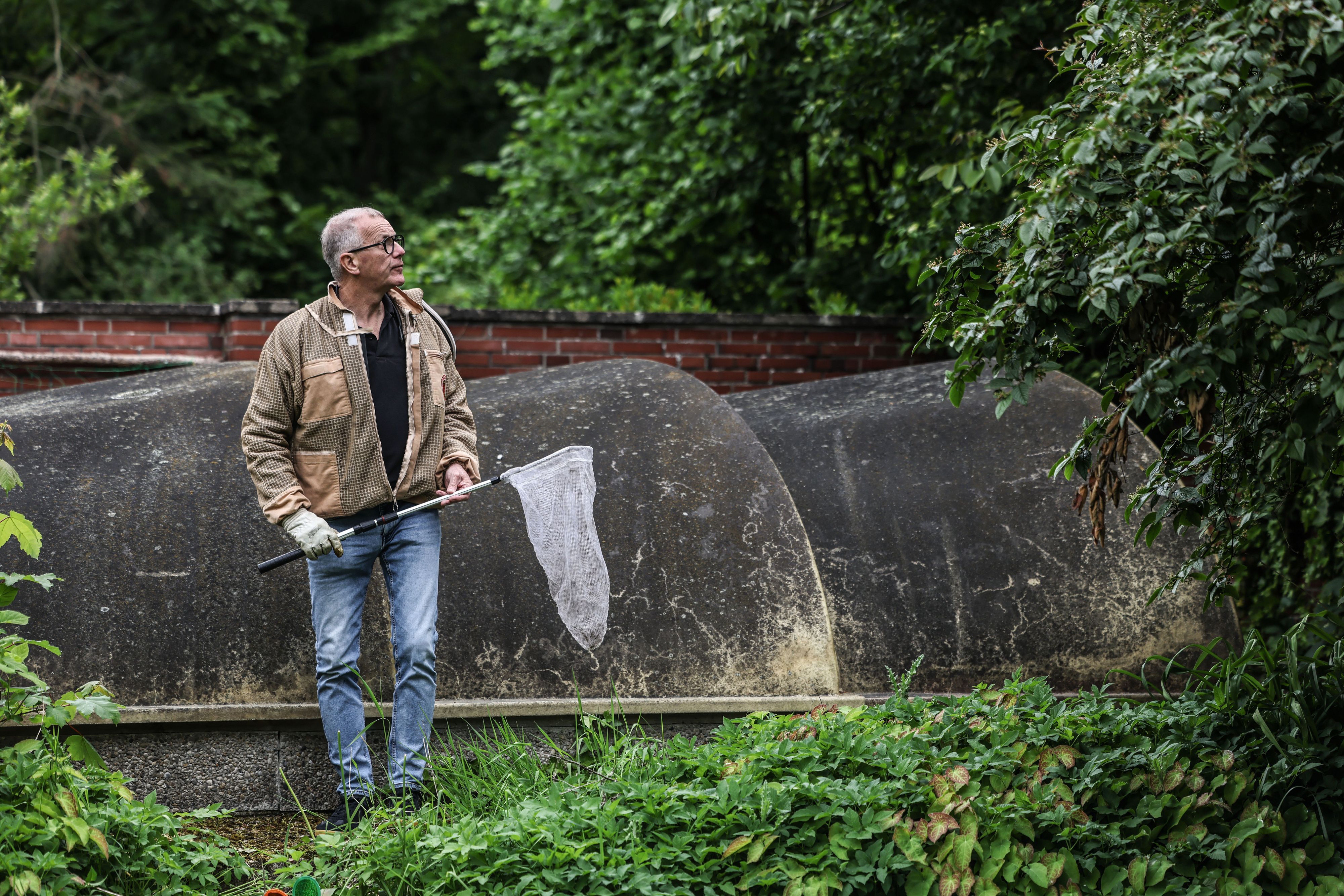 Ralf Atzorn, Vorsitzender des Kölner Imkerverbands, steht mit einem Kescher in einem Garten.