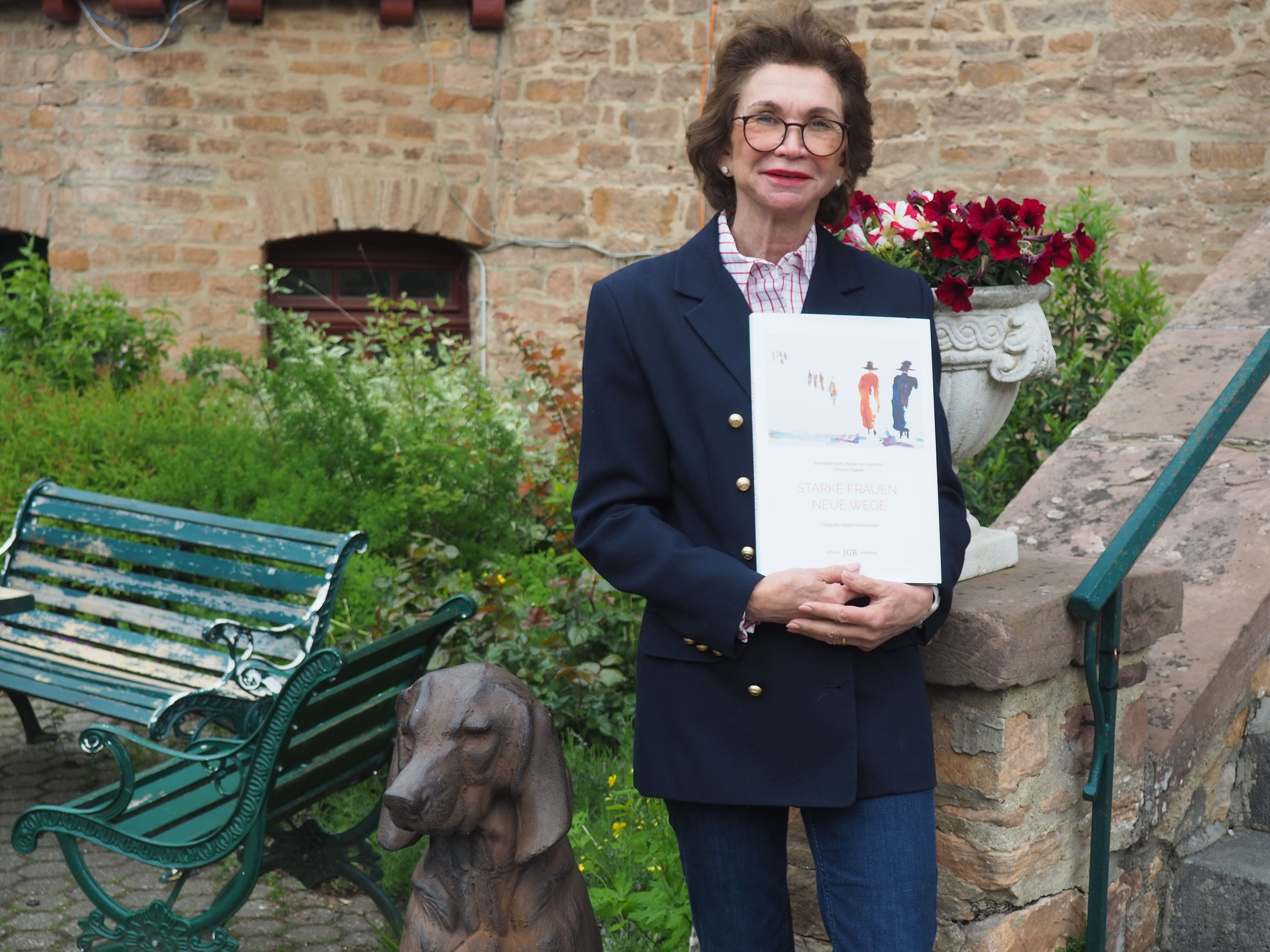 Jeannette Gräfin Beissel steht an der Treppe zur Burg und hält ihr Buch in den Händen.