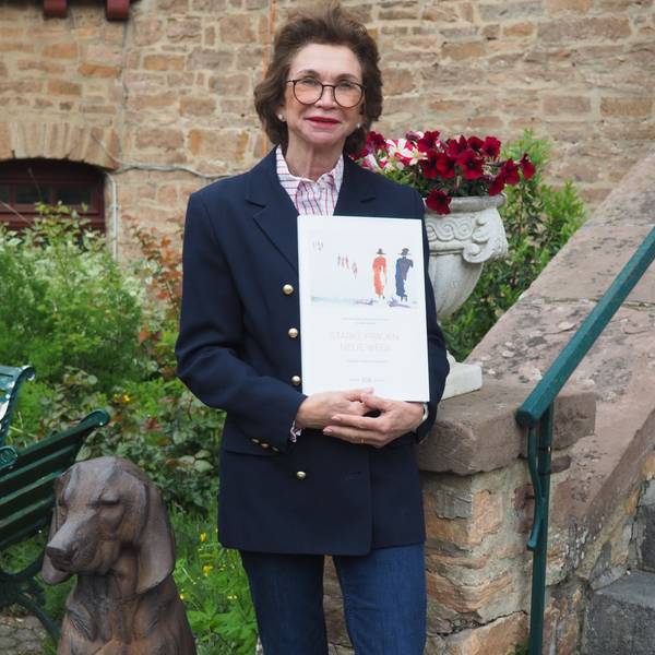 Jeannette Gräfin Beissel steht an der Treppe zur Burg und hält ihr Buch in den Händen.