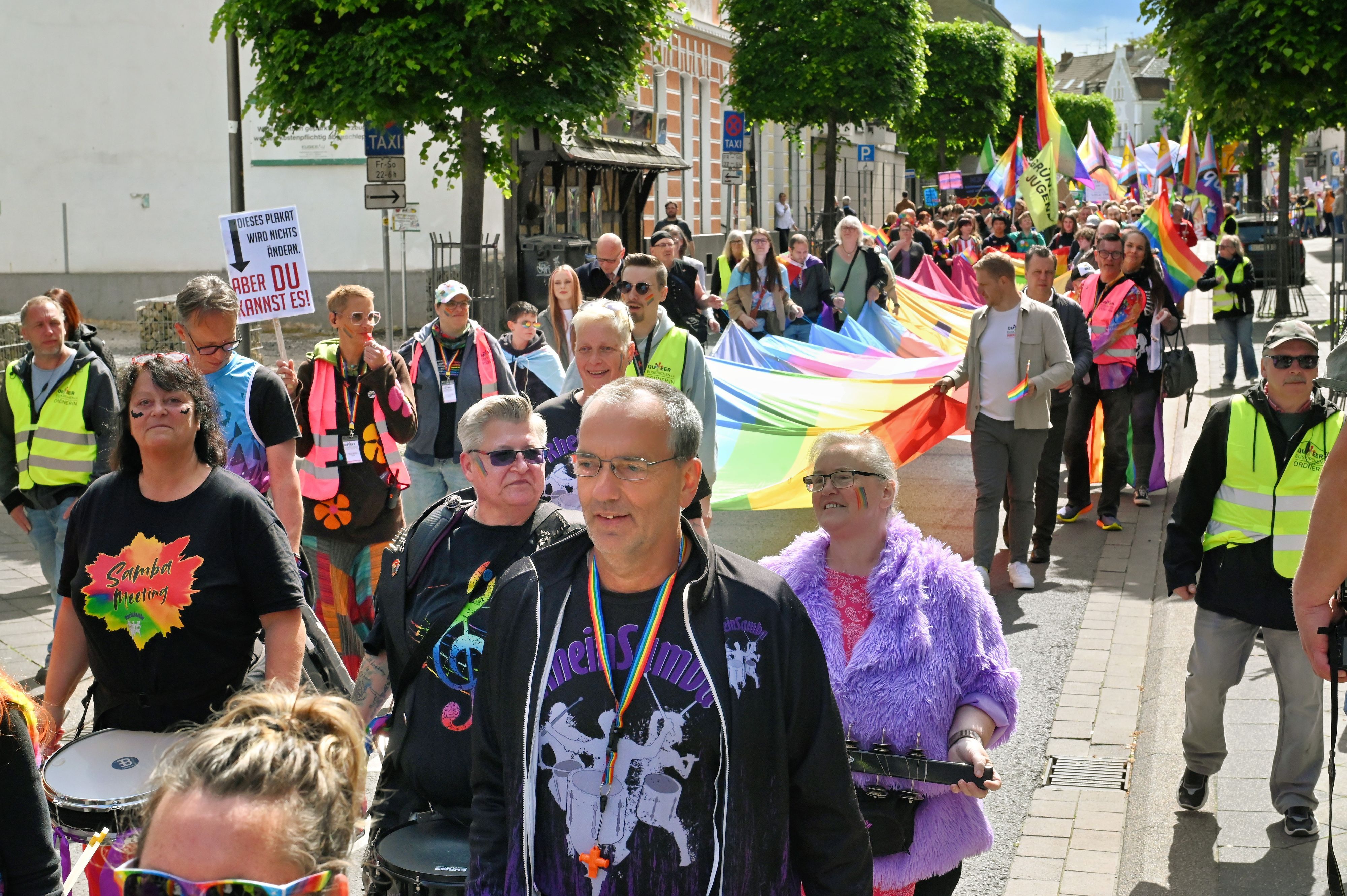 Farbenfroh gekleidet zieht die lange Parade durch die Innenstadt. Mehrere Leute, darunter auch der Landrat und der Bürgermeister, tragen die große Pride-Flagge.