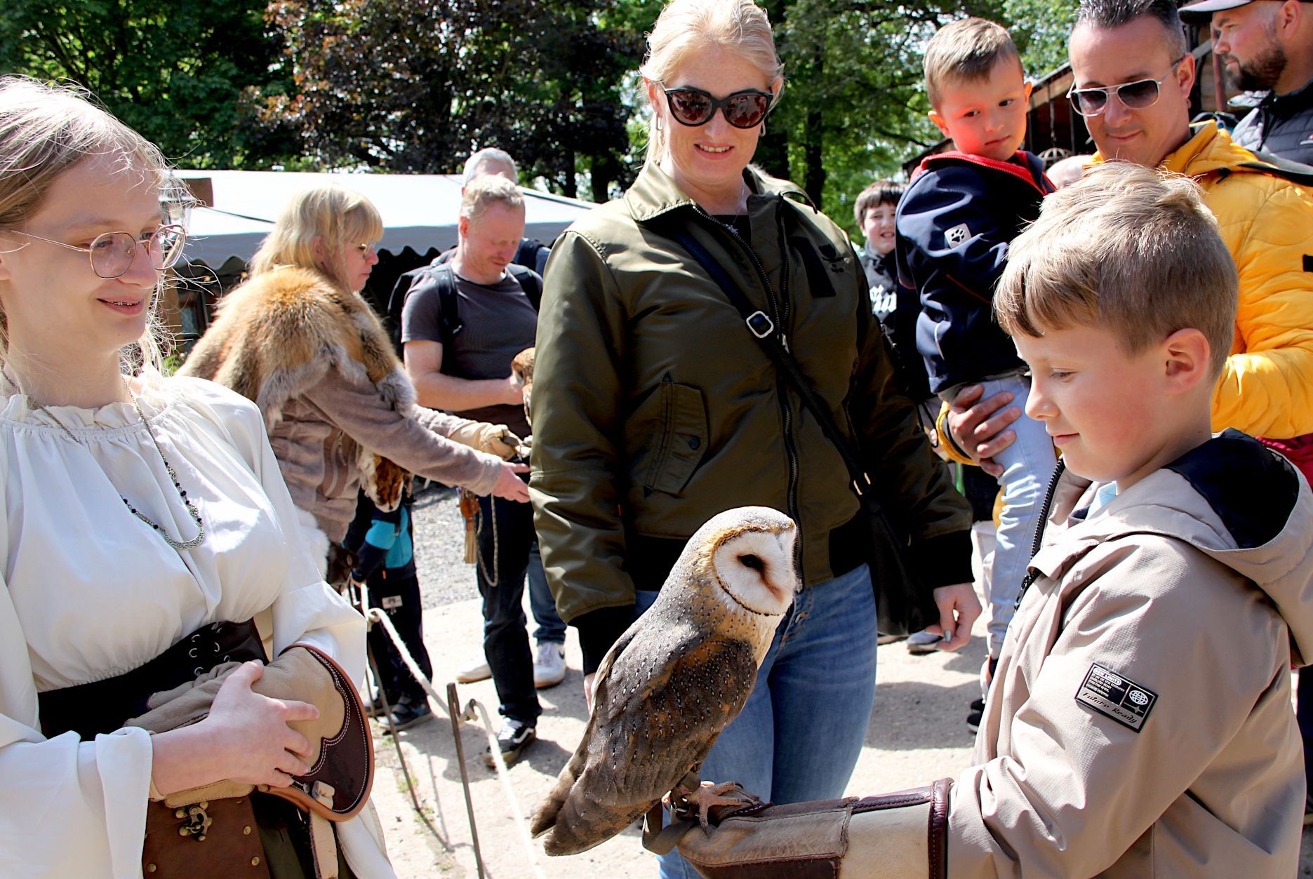 Der Junge hält auf seinem Handschuh die Schleiereule, während die mittelalterlich gekleidete Falknerin aufpasst.