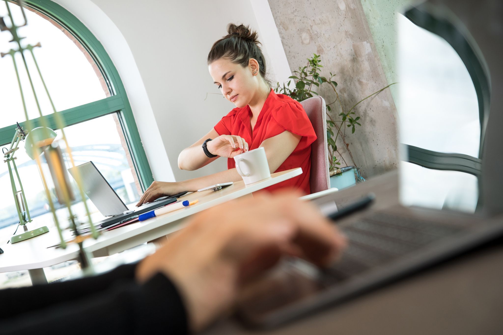 Frau schaut an ihrem Arbeitsplatz auf die Uhr