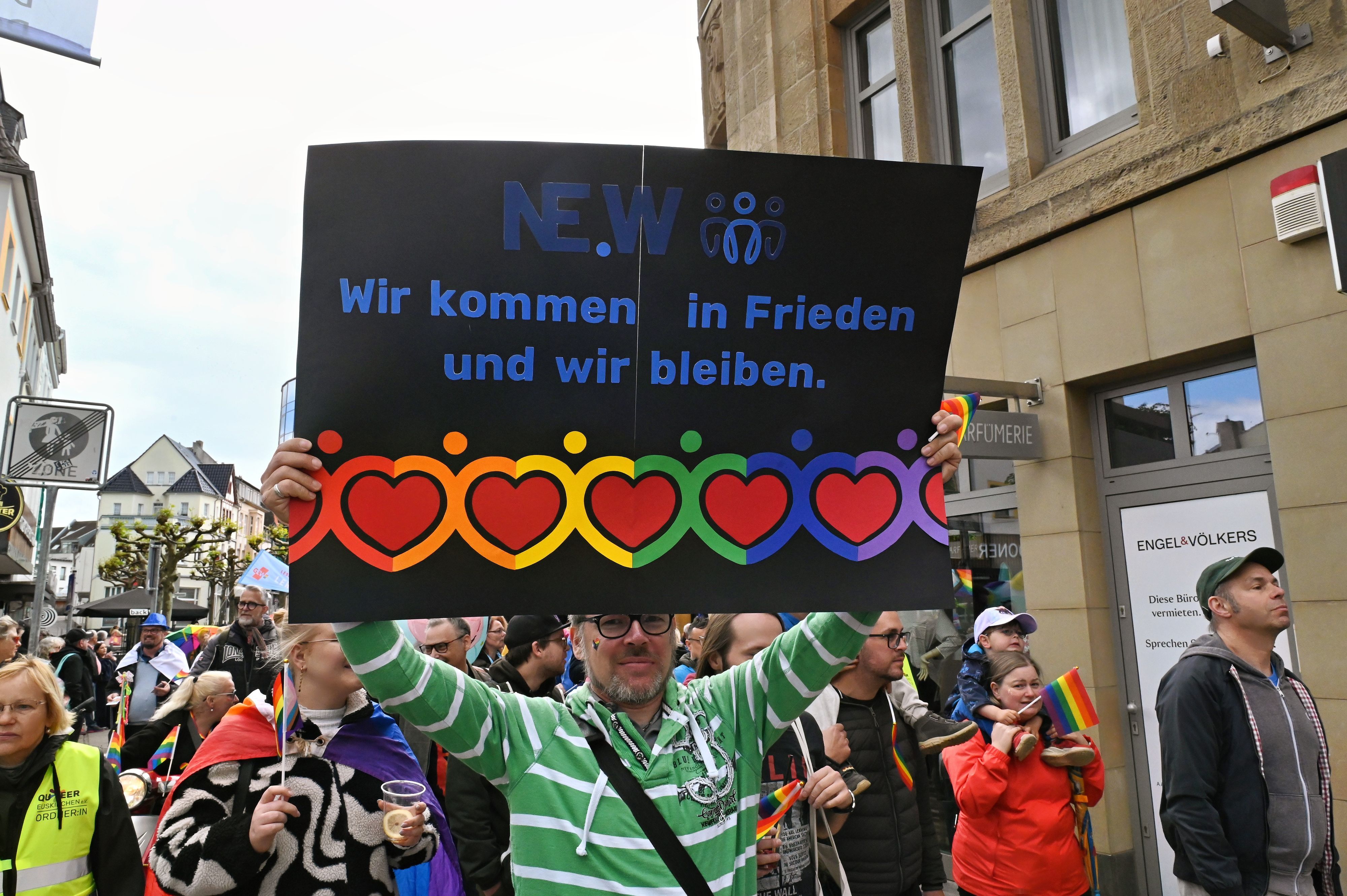 Ein Mann mit grün-weiß gestreiftem Shirt hält die schwarze Tafel mit dem Motto und zahlreichen farbenfrohen Herzen hoch.