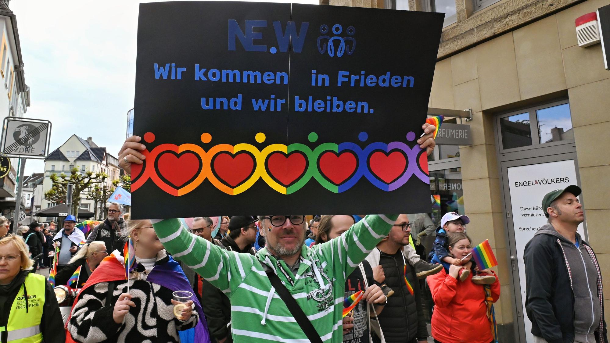 Ein Mann mit grün-weiß gestreiftem Shirt hält die schwarze Tafel mit dem Motto und zahlreichen farbenfrohen Herzen hoch.