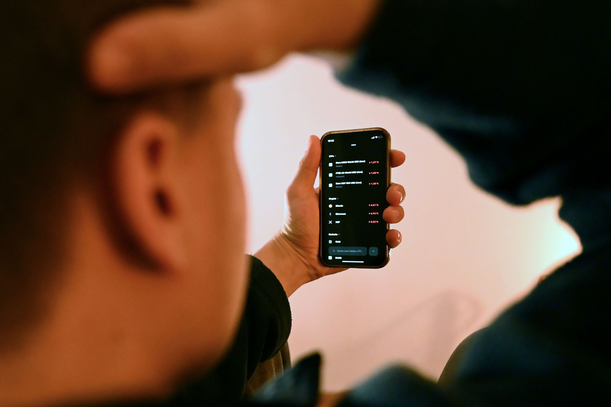 Mann schaut sich Trading-App eines Neobrokers mit Aktienkursen an