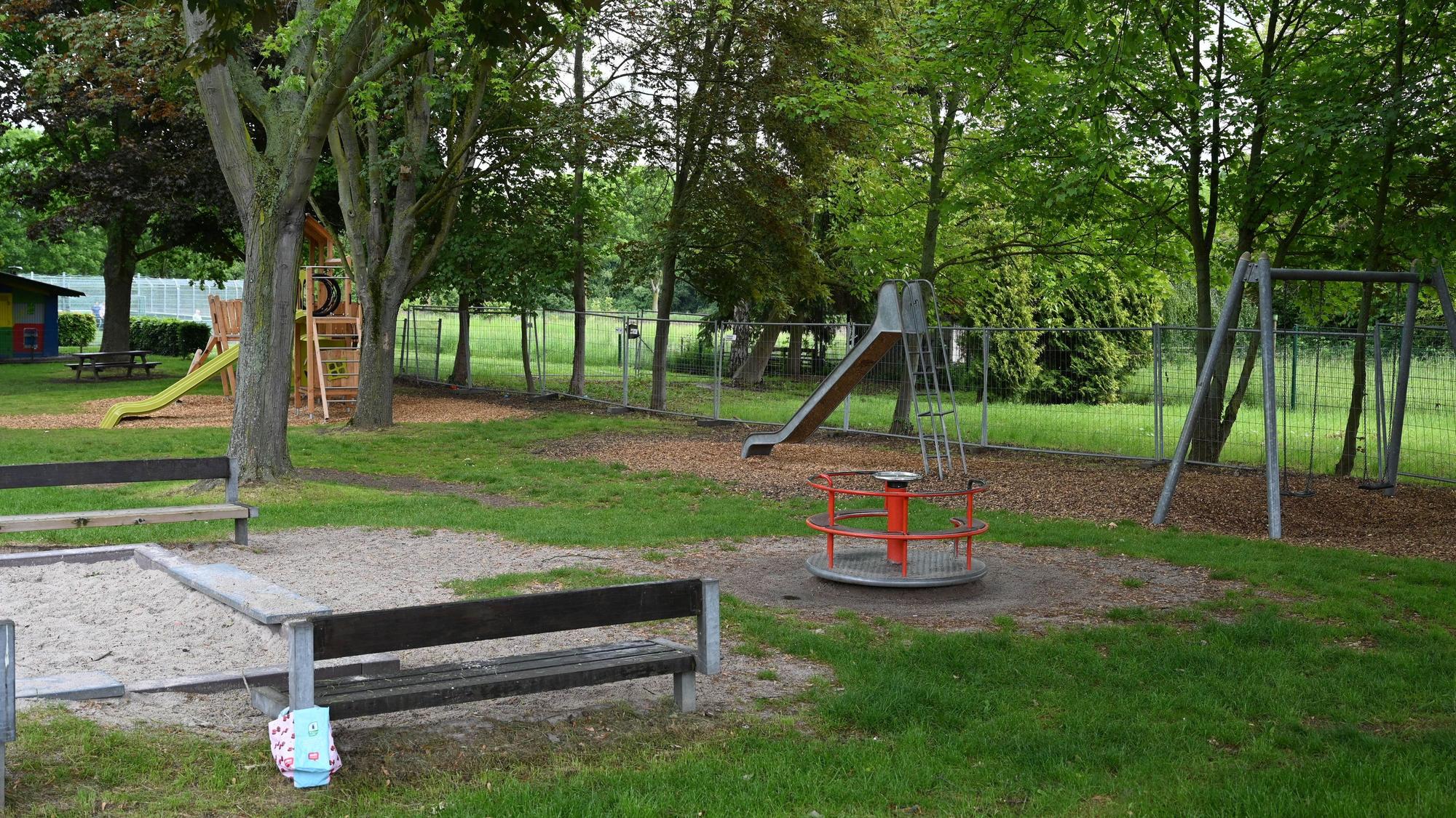 Das Bild zeigt den Spielplatz: Sandkasten, Bänke, Rutschen. Im Hintergrund ein Bauzaun, der auf die Erweiterung hinweist.
