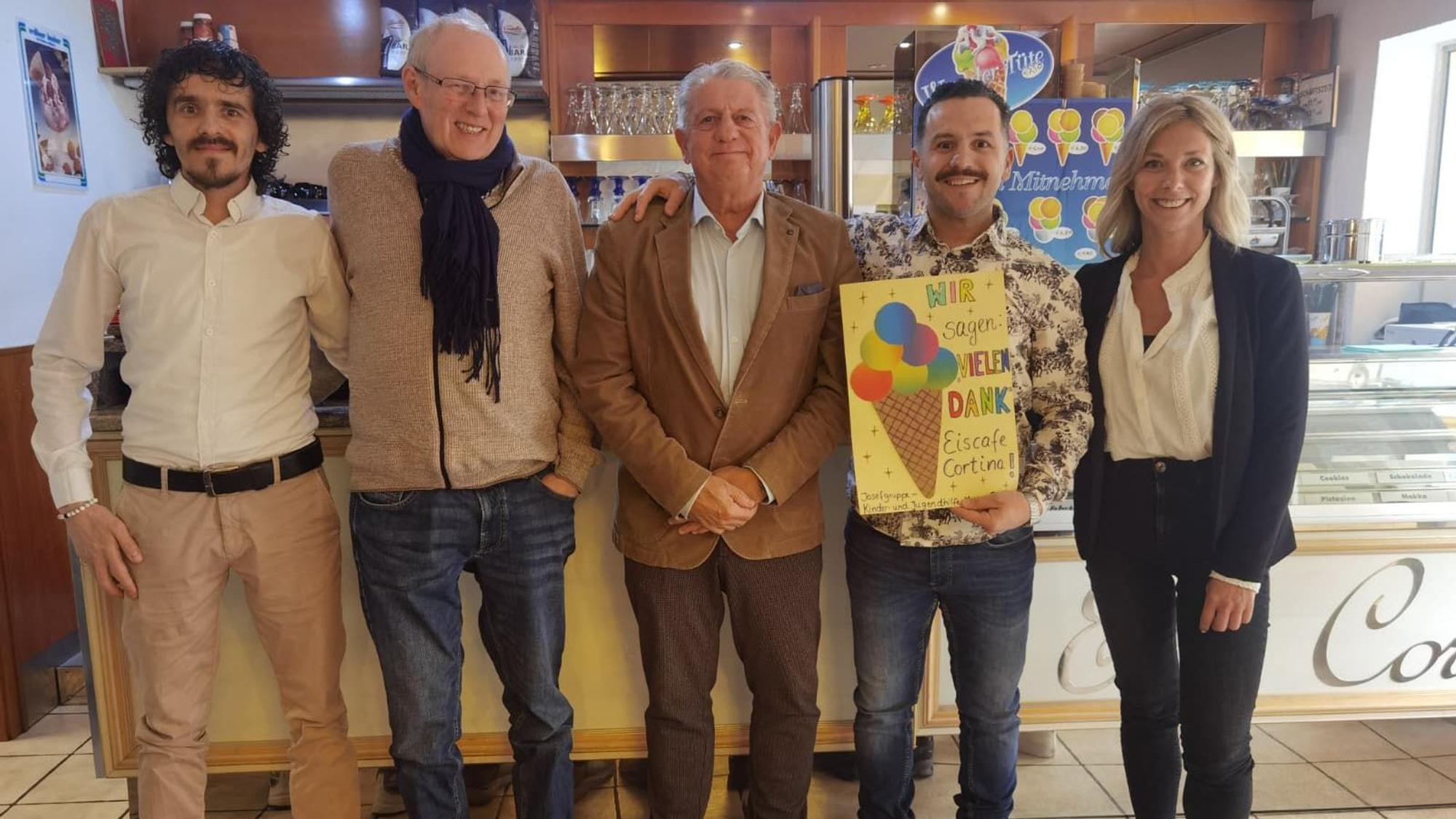 Eine Frau und vier Männer stehen nebeneinander und lächeln. Ein Mann hält ein gebasteltes Plakat vor sich.