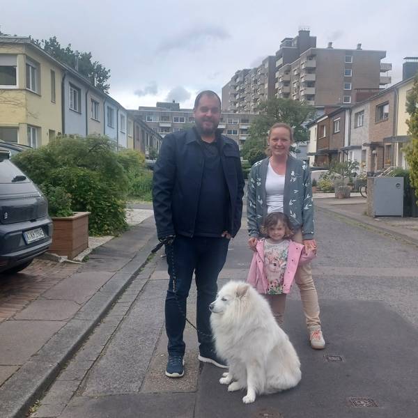 Ein Mann, eine Frau, ein Kind und ein Hund stehen auf einer schmalen Anwohnerstraße.