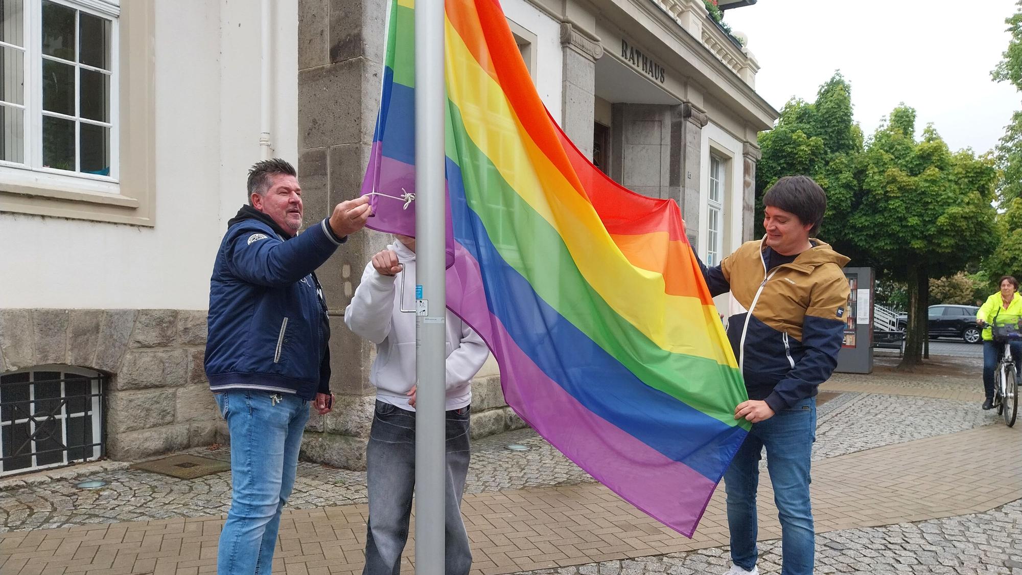 Drei Männer hissen eine Regenbogenfahne.