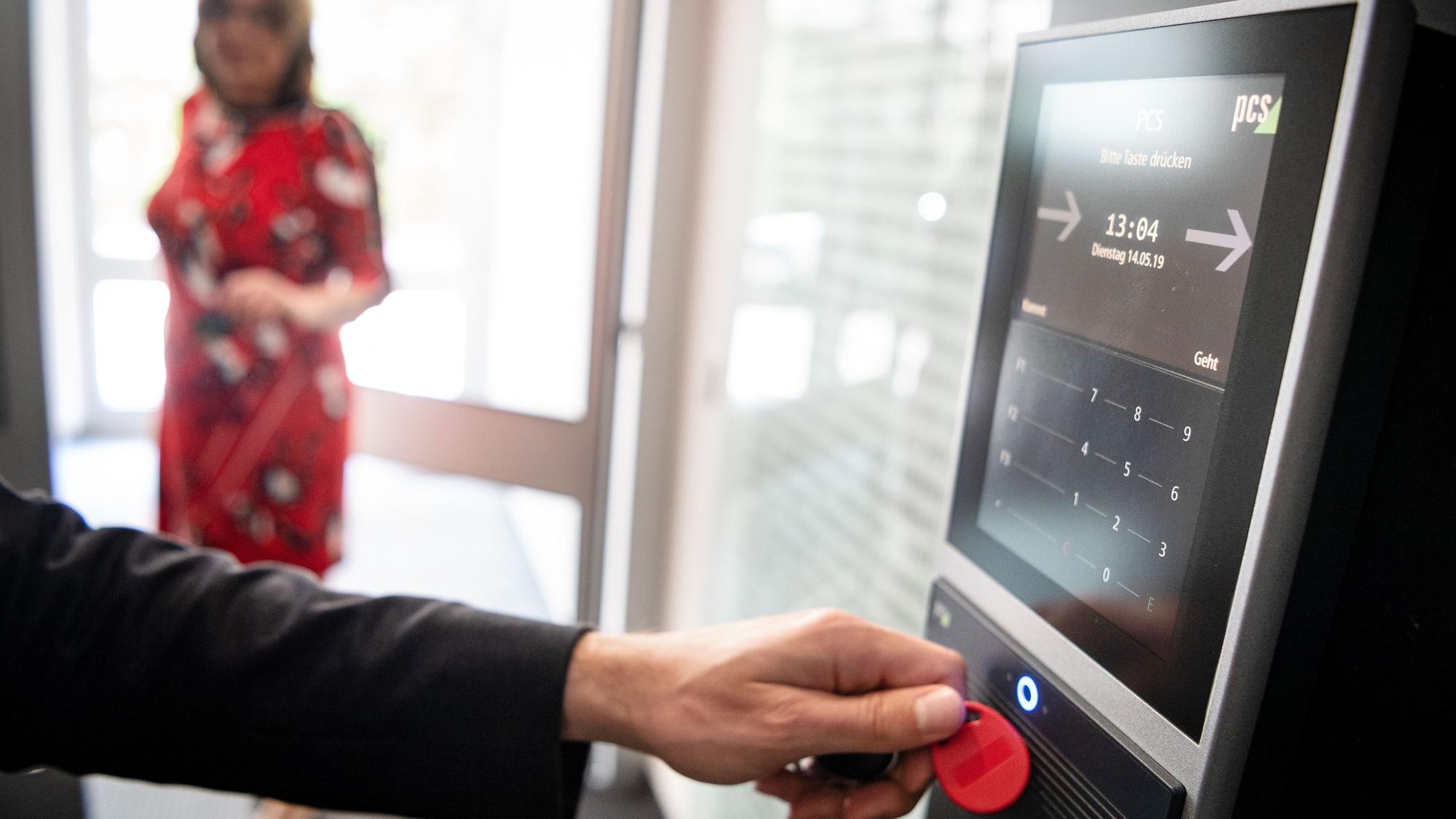 Eine Person hält einen roten Chip an ein Computer-Lesegerät um ihre Arbeitszeit zu erfassen.