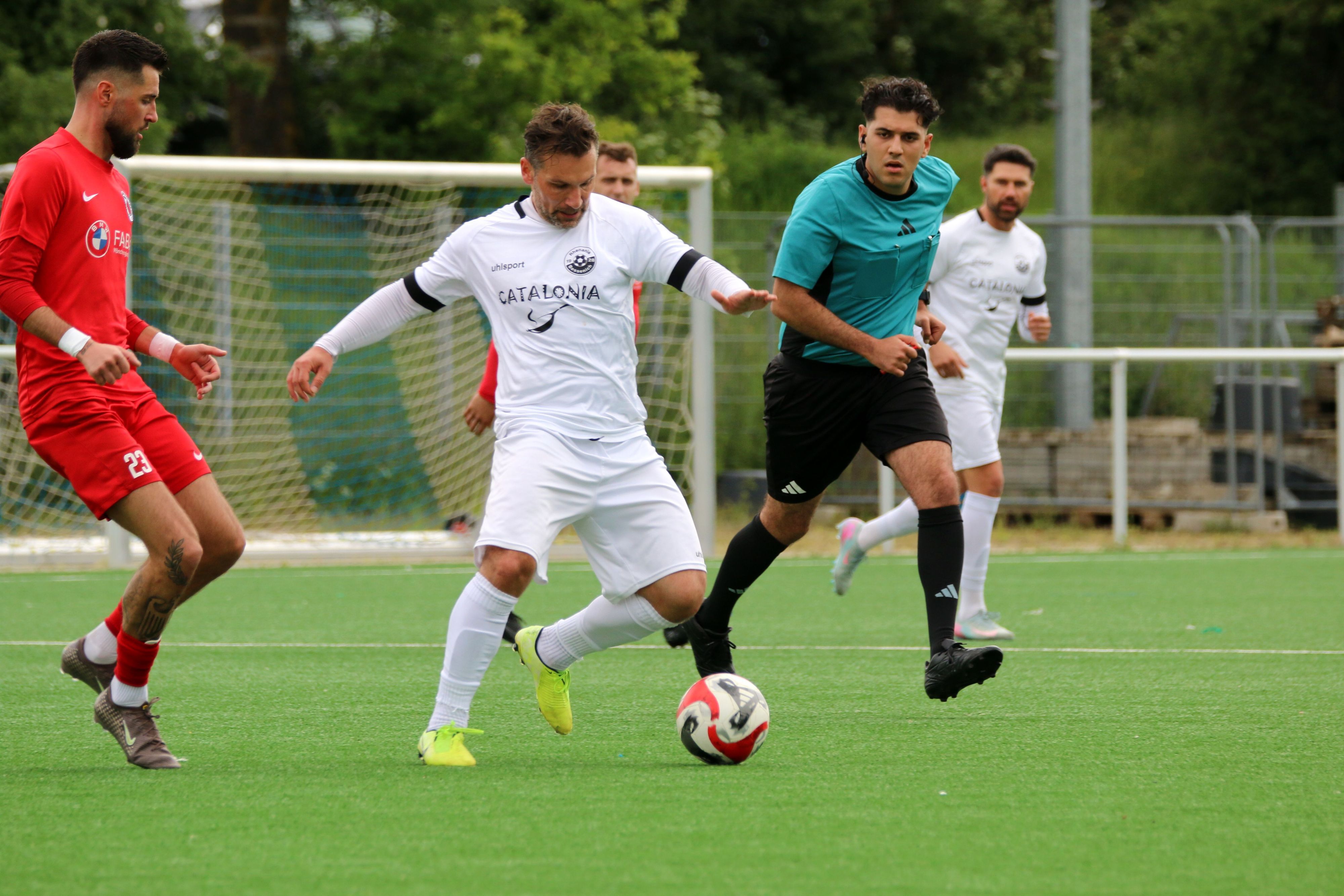 Athanasios Noutsos ist am Ball, ein Gegenspieler nähert sich ihm. Hinter ihm hat der Schiedsrichter alles im Blick.