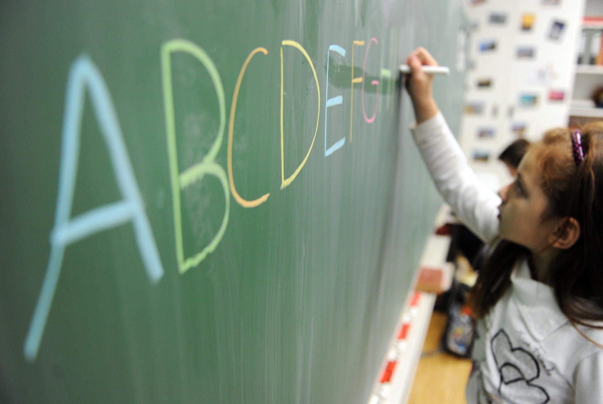 Ein Mädchen schreibt das ABC an die Tafel. In NRW sollen Kinder künftig besser auf die Einschulung vorbereitet werden.