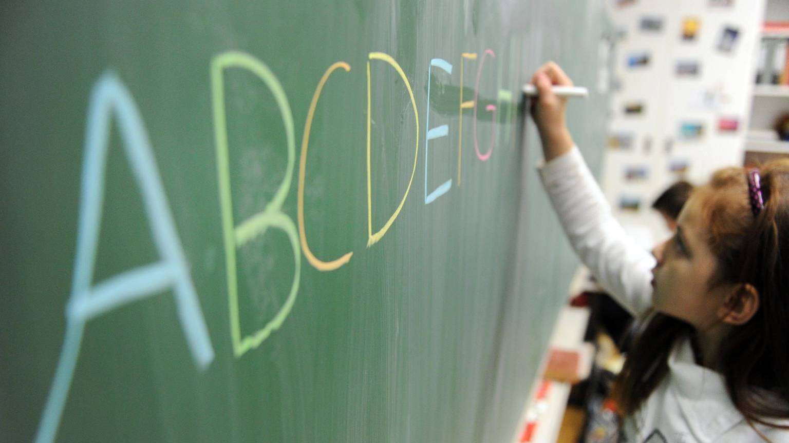 Ein Mädchen schreibt das ABC an die Tafel. In NRW sollen Kinder künftig besser auf die Einschulung vorbereitet werden.