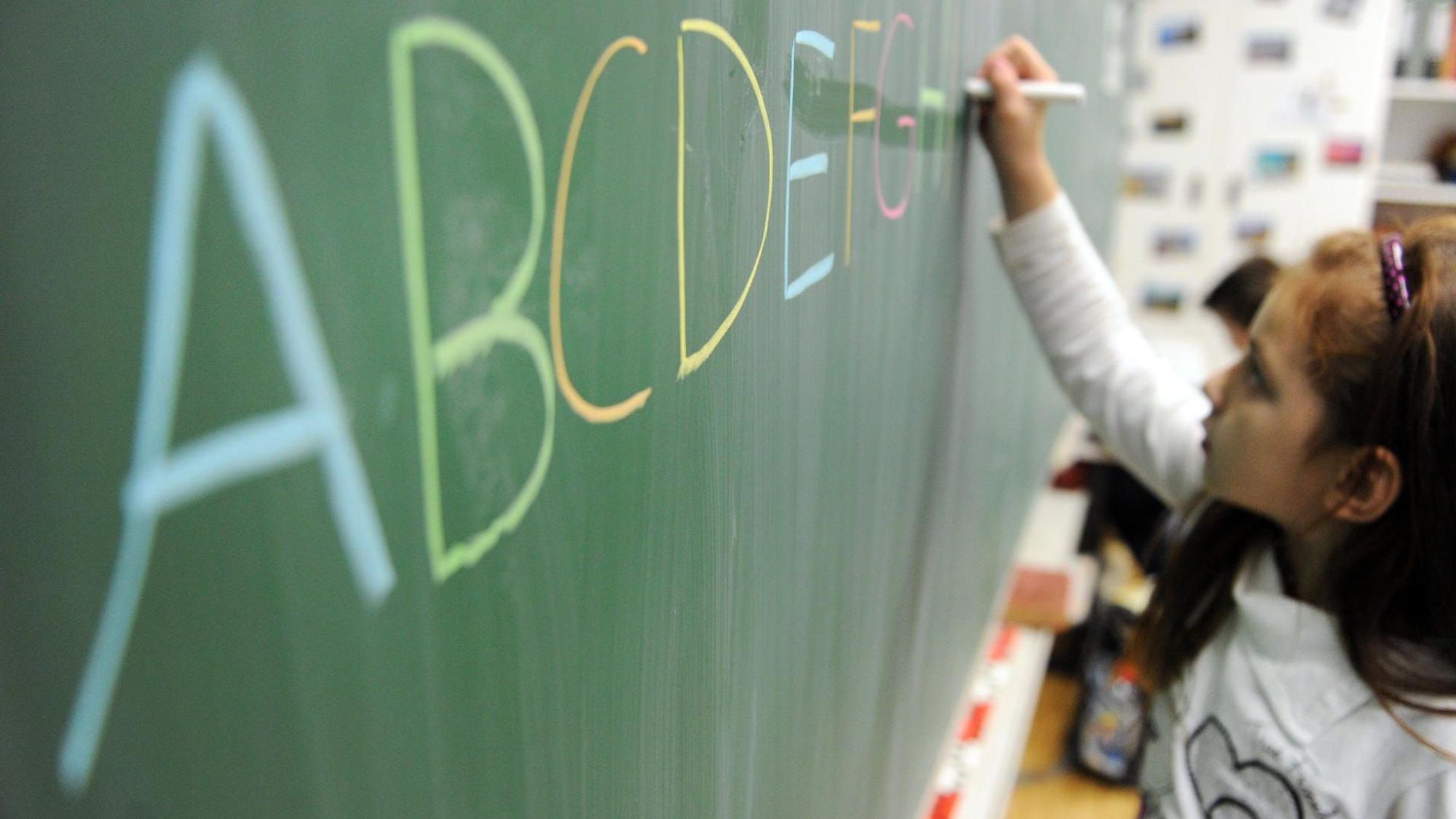 Ein Mädchen schreibt das ABC an die Tafel. In NRW sollen Kinder künftig besser auf die Einschulung vorbereitet werden.
