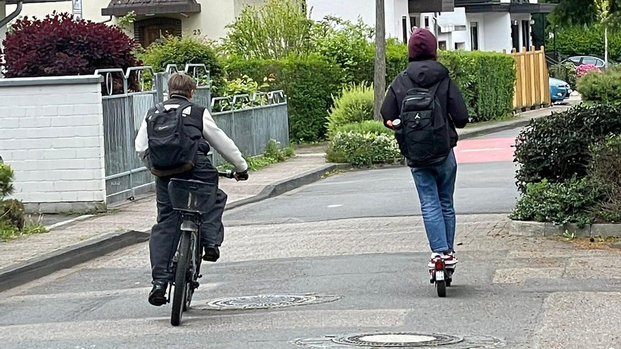 Ein Junge faährt auf dem Farrad, ein Junge auf dem Roller.