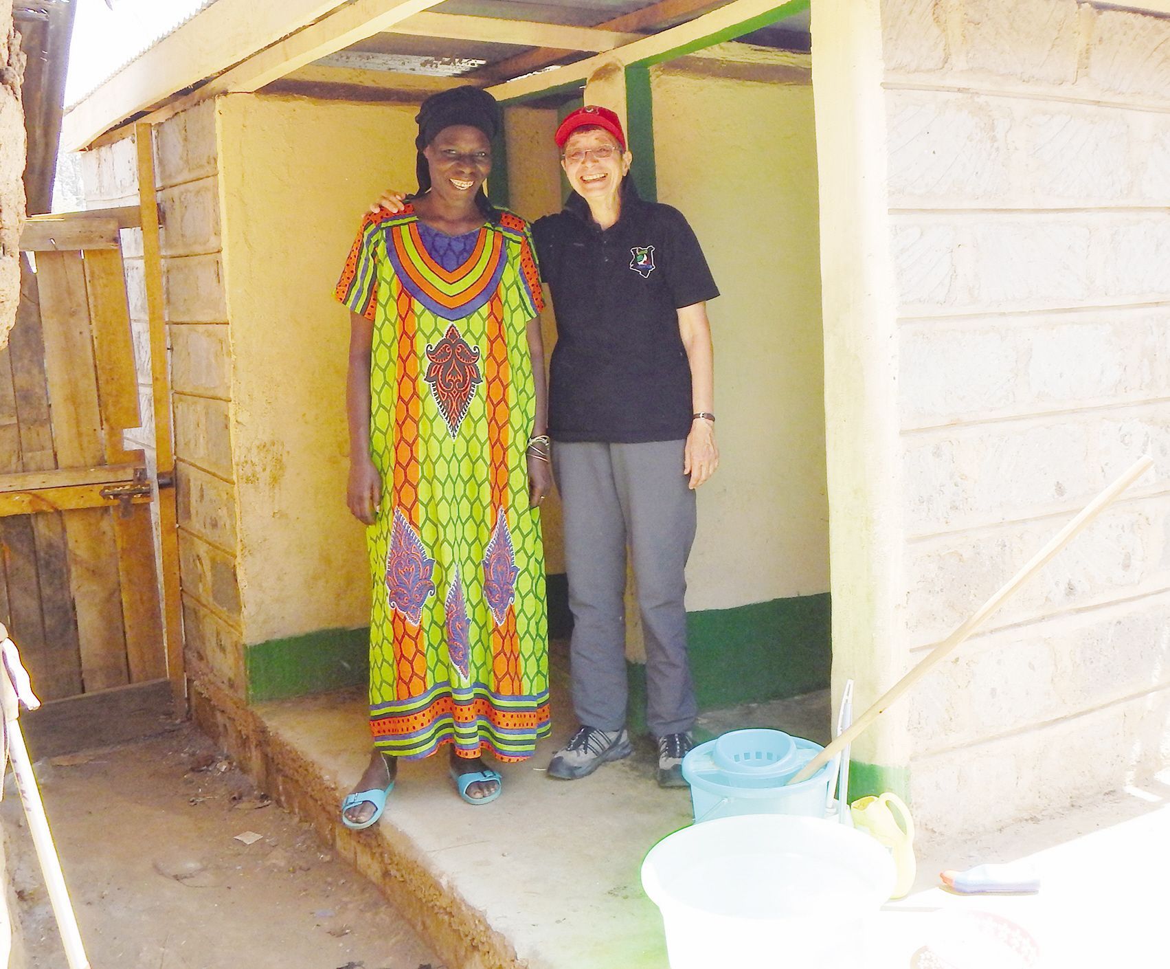 Eine Frau mit Schirmmütze legt den Arm um eine Afrikanerin im bunten Kleid.