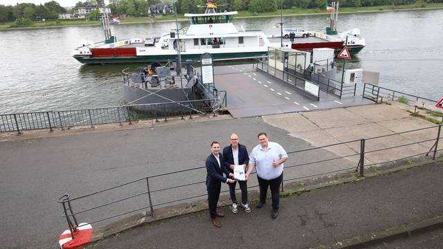 Drei Männer stehen vor der Rheinfähre Königswinter, die gerade abgelegt hat.