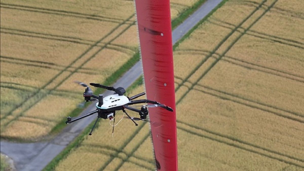 Dieses Foto zeigt, wie die schwarzweiße Drohne das rote Rotorblatt einer Windenergieanlage anfliegt.