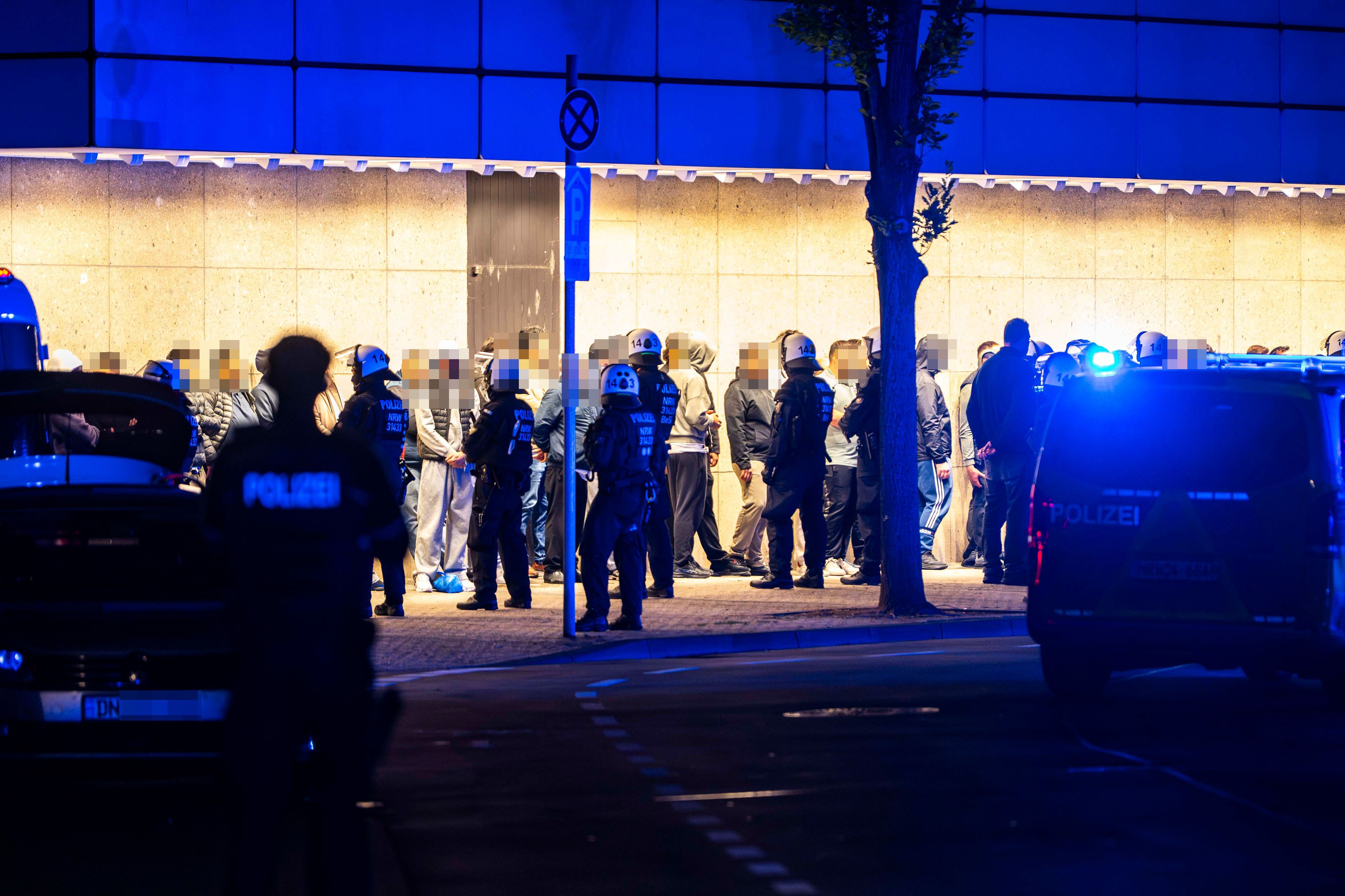 Das Bild zeigt zahlreiche Menschen, die mutmaßlich an der Schlägerei beteiligt waren. Sie werden von Polizeibeamten bewacht.