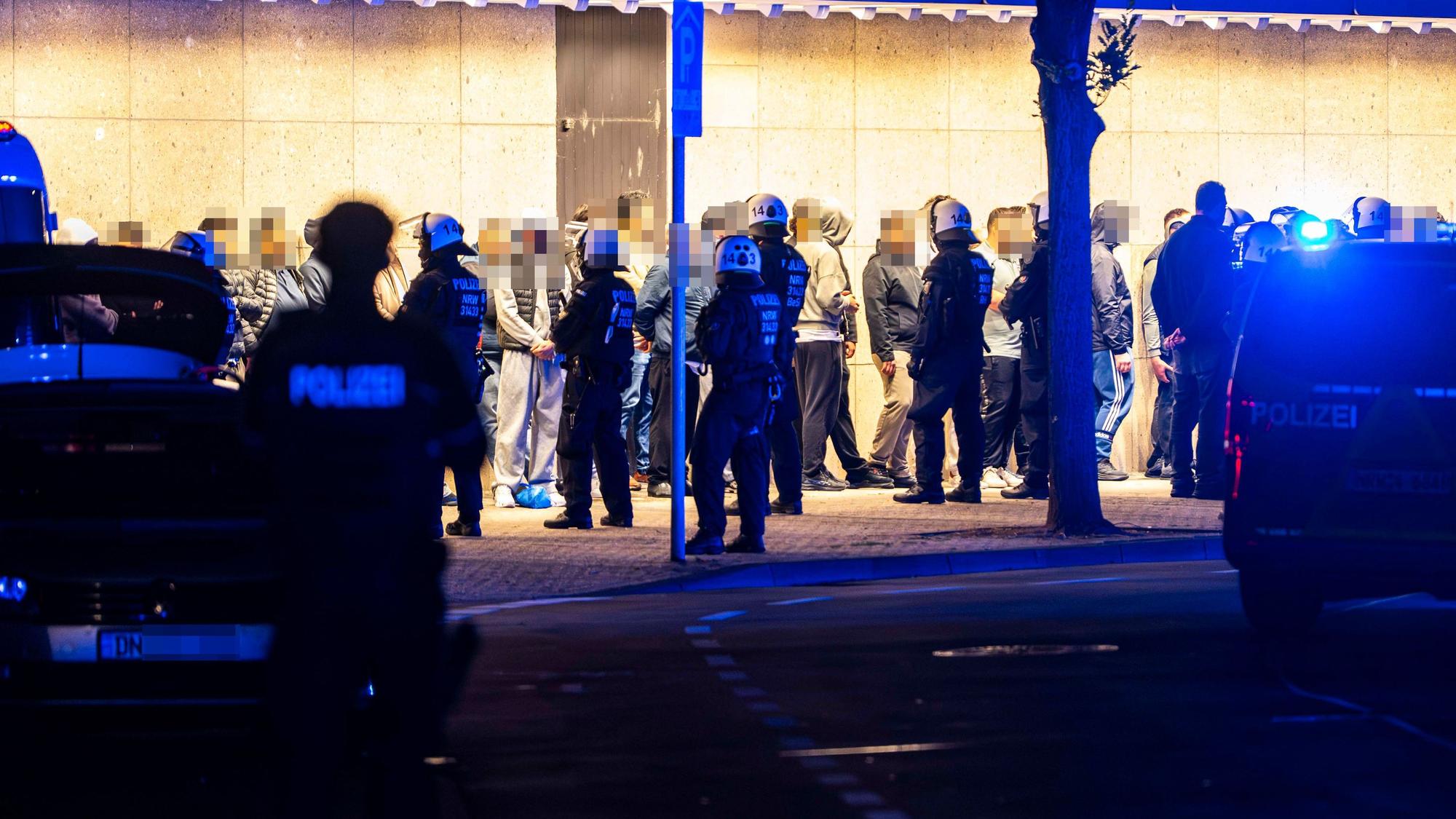Das Bild zeigt zahlreiche Menschen, die mutmaßlich an der Schlägerei beteiligt waren. Sie werden von Polizeibeamten bewacht.