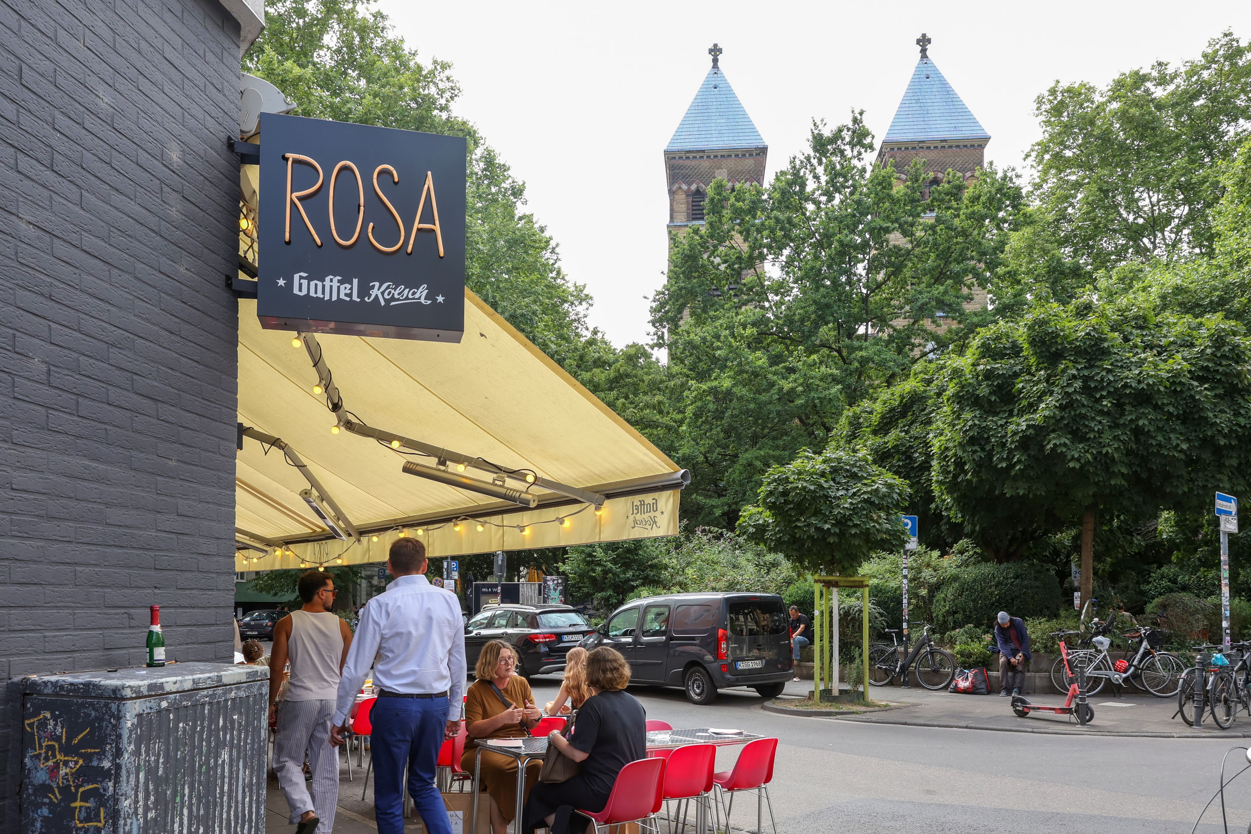 Ein Schild von der Bar Rosa, dahinter die zwei Türme der Kirche St. Michael.