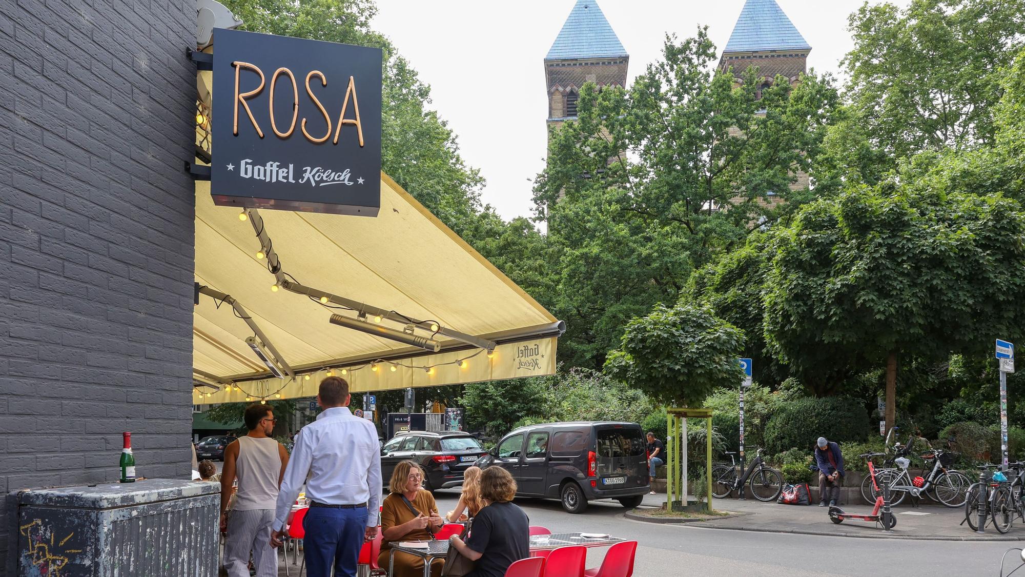 Ein Schild von der Bar Rosa, dahinter die zwei Türme der Kirche St. Michael.
