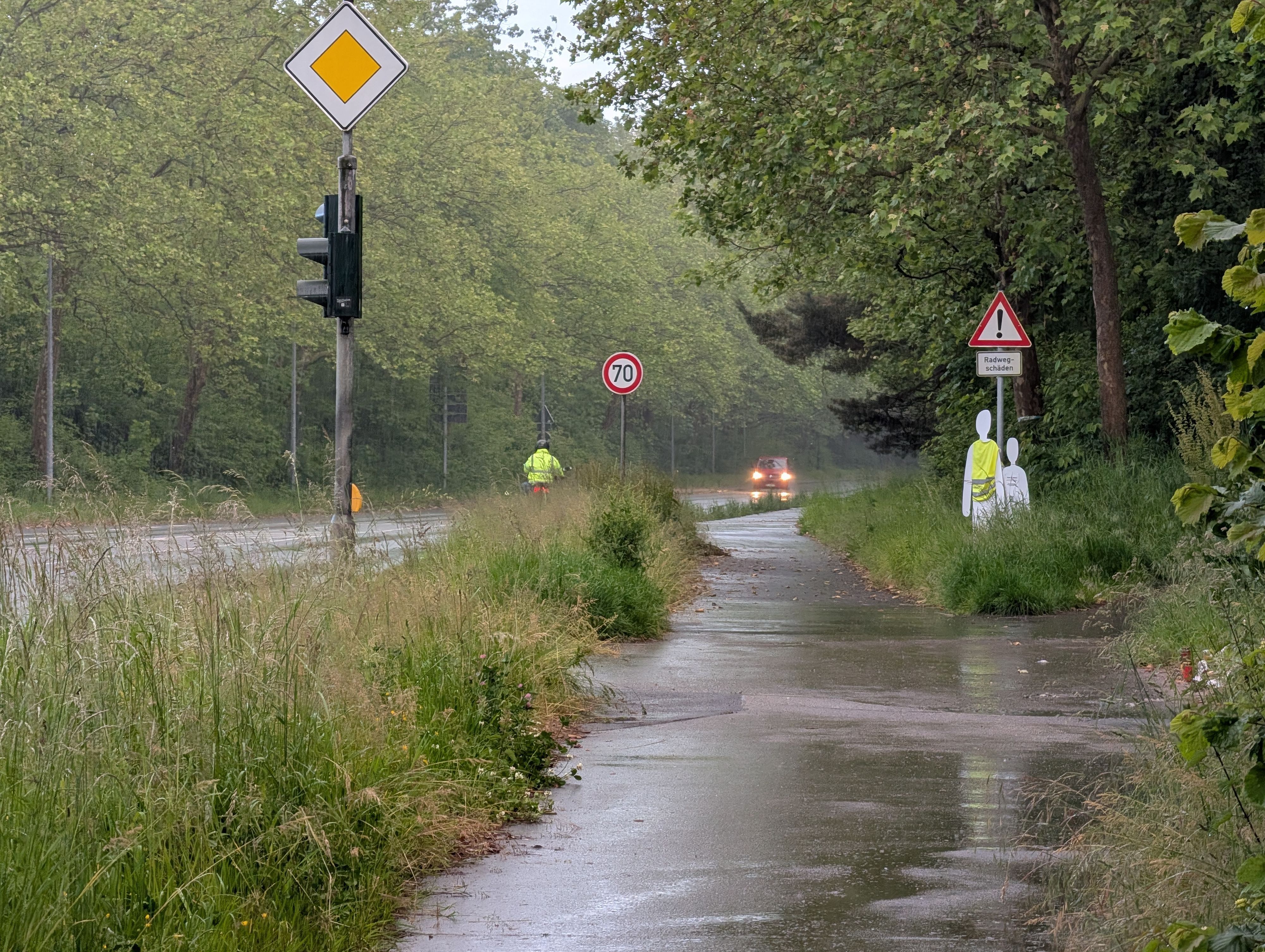 Das Foto zeig die hochgewachsene Vegetation, im Hintergrund die Gedenkstätte für die beiden jungen Unfallopfer.
