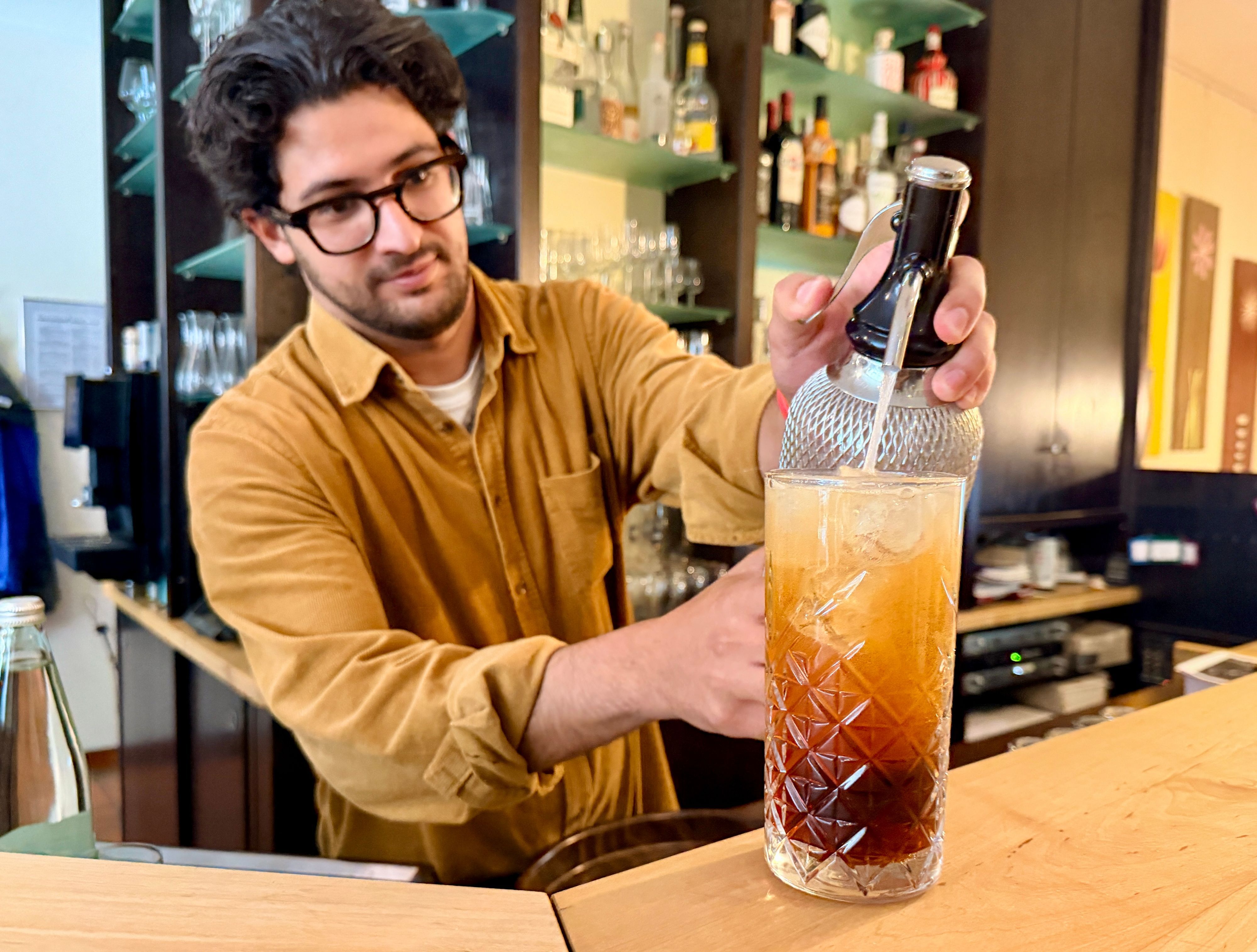 Ali Hassan steht hinter der Theke und befüllt ein Glas mit Soda.