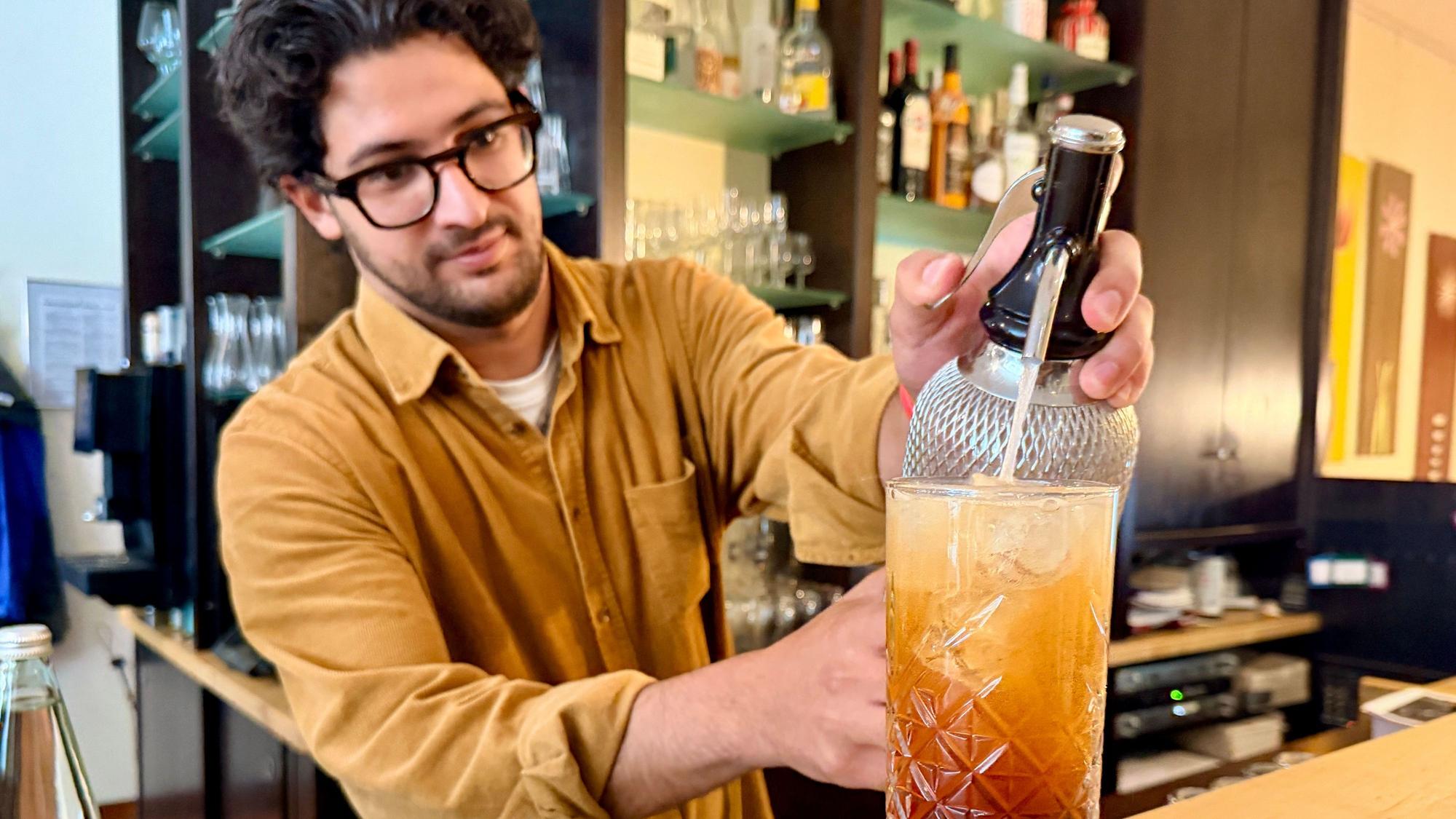 Ali Hassan steht hinter der Theke und befüllt ein Glas mit Soda.