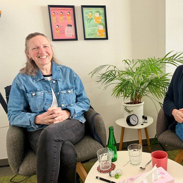 Die beiden Frauen sitzen auf Stühlen nebeneinander und lächeln in Richtung Kamera.