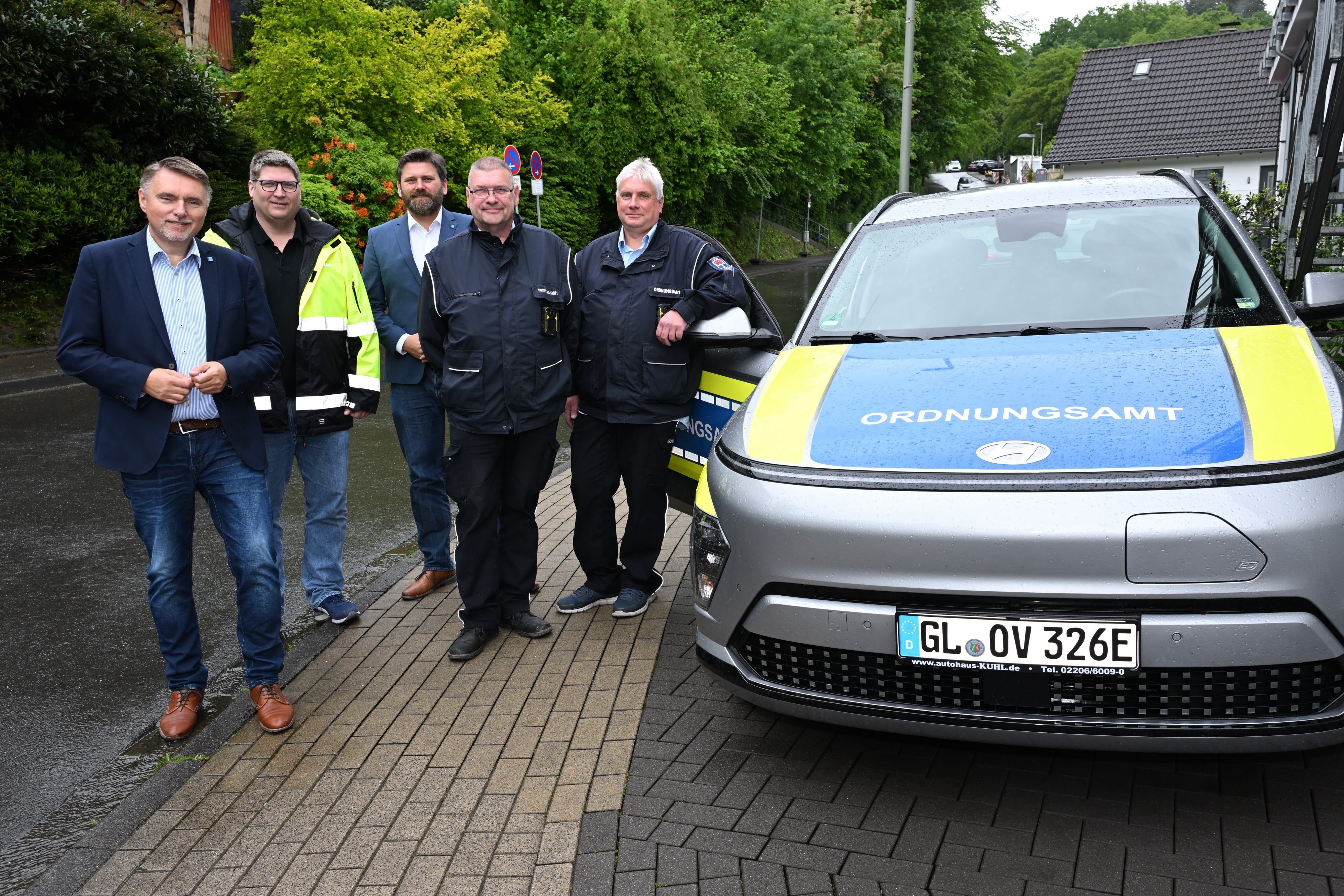 Fünf Männer stehen nebeneinander und neben einem Ordnungsamt-Wagen.