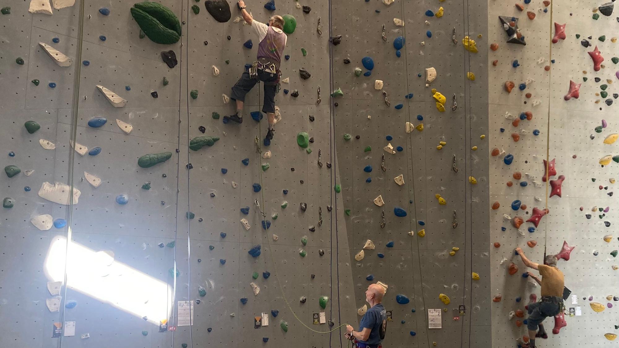 Auf dem Bild sind drei Männer an einer Kletterwand zu sehen.