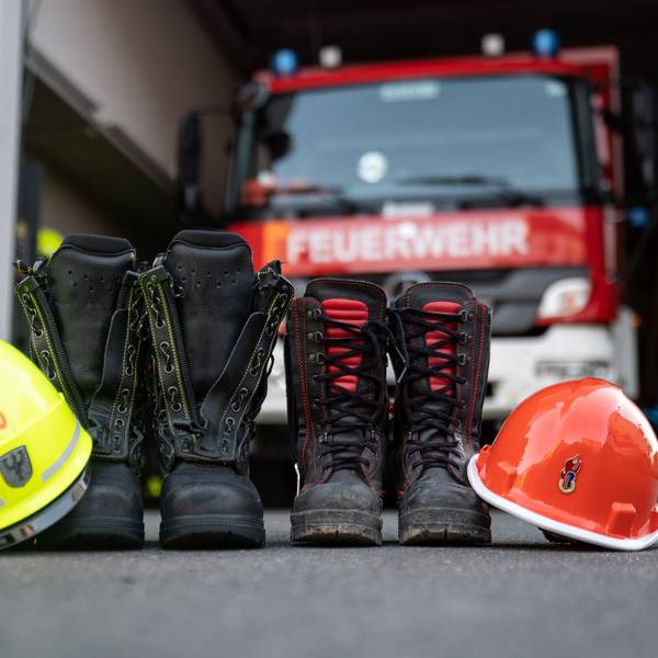 Stiefel und Helm eines Mitglieds der Jugendfeuerwehr und einem erwachsenen Mitglied der Freiwilligen Feuerwehr Frankfurt-Seckbach stehen vor einem Feuerwehrhaus.