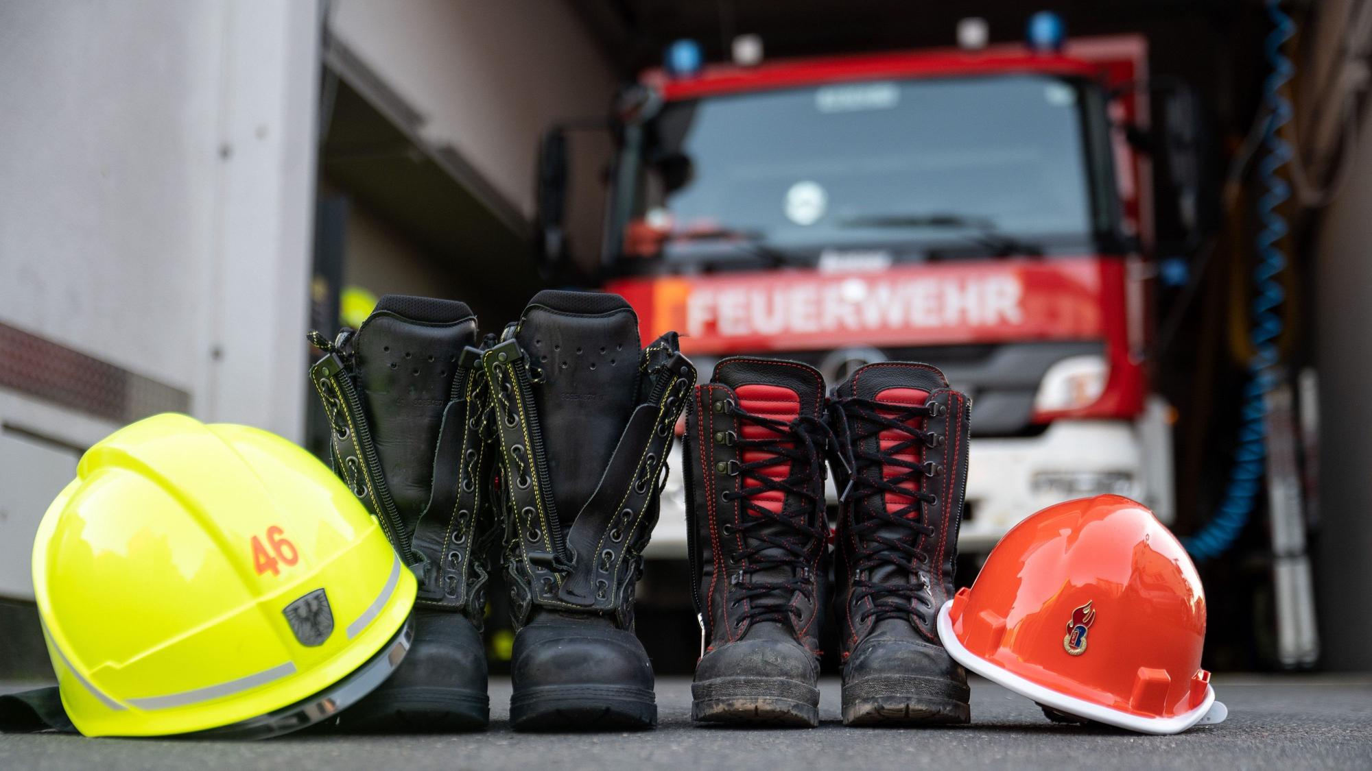 Stiefel und Helm eines Mitglieds der Jugendfeuerwehr und einem erwachsenen Mitglied der Freiwilligen Feuerwehr Frankfurt-Seckbach stehen vor einem Feuerwehrhaus.
