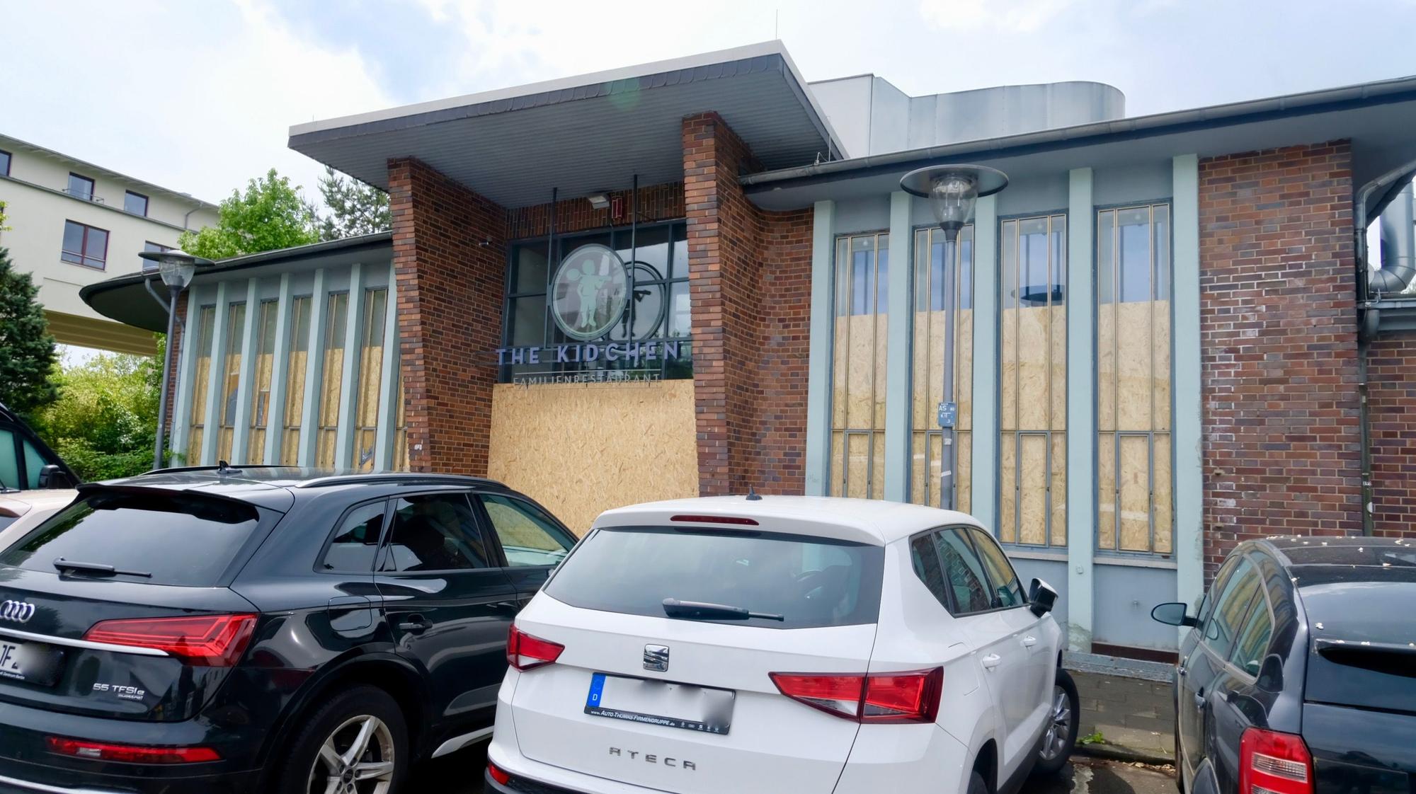 Vor einer Halle stehen geparkte Autos.