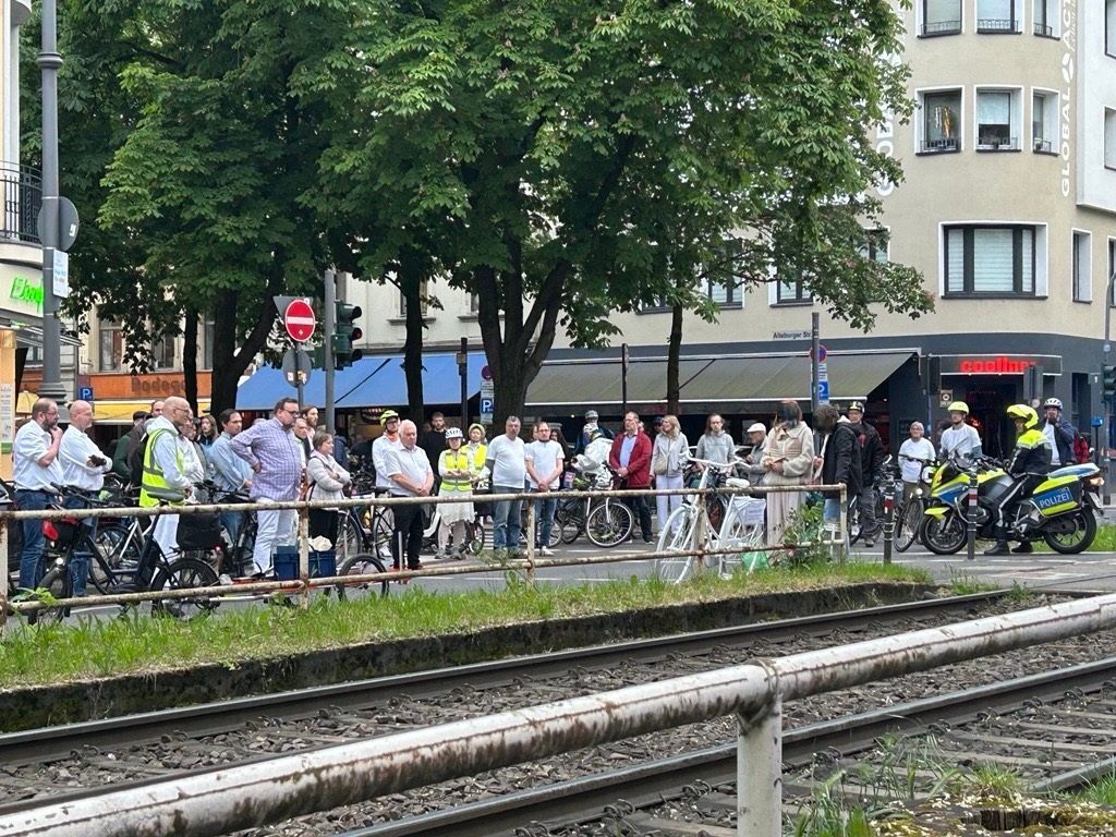 Zahlreiche Menschen stehen vor einem weißen Fahrrad, das an einem Bahnübergang steht.