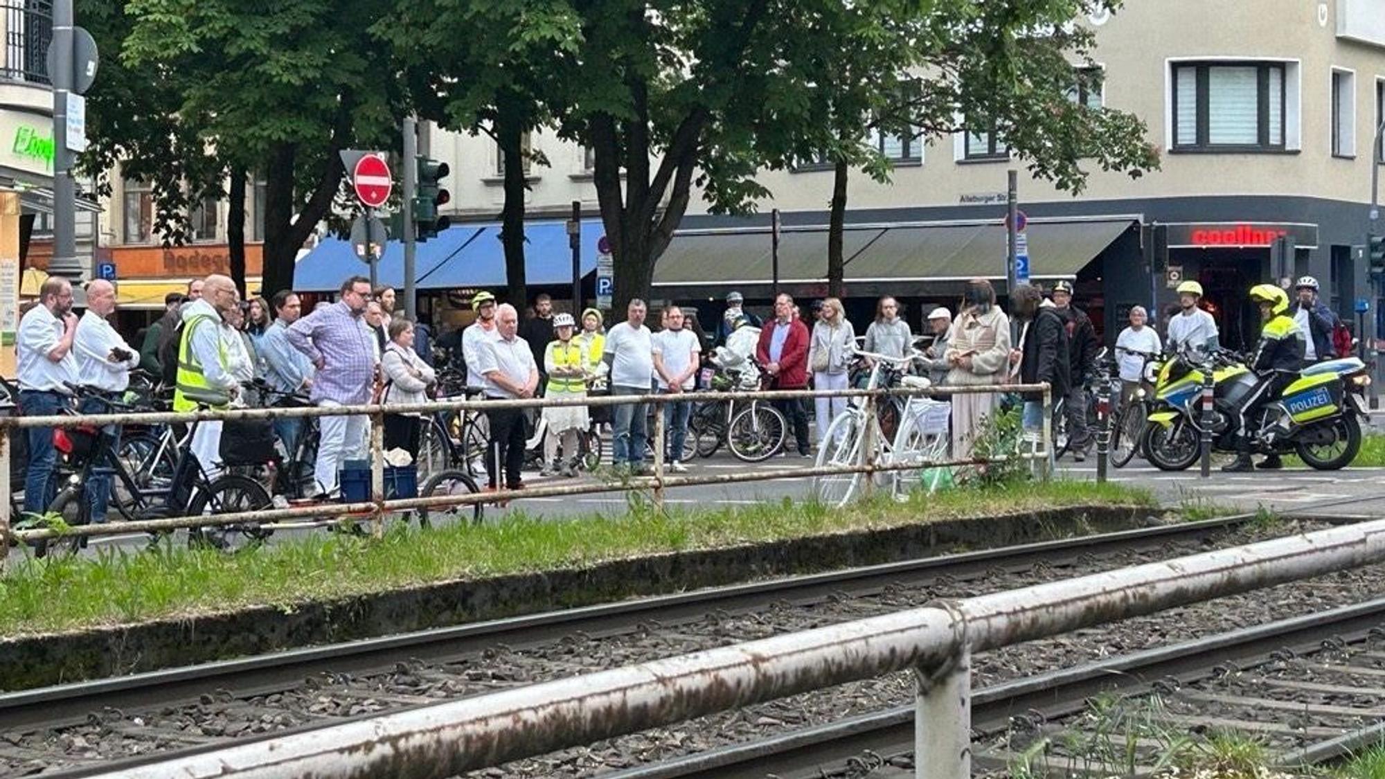 Zahlreiche Menschen stehen vor einem weißen Fahrrad, das an einem Bahnübergang steht.