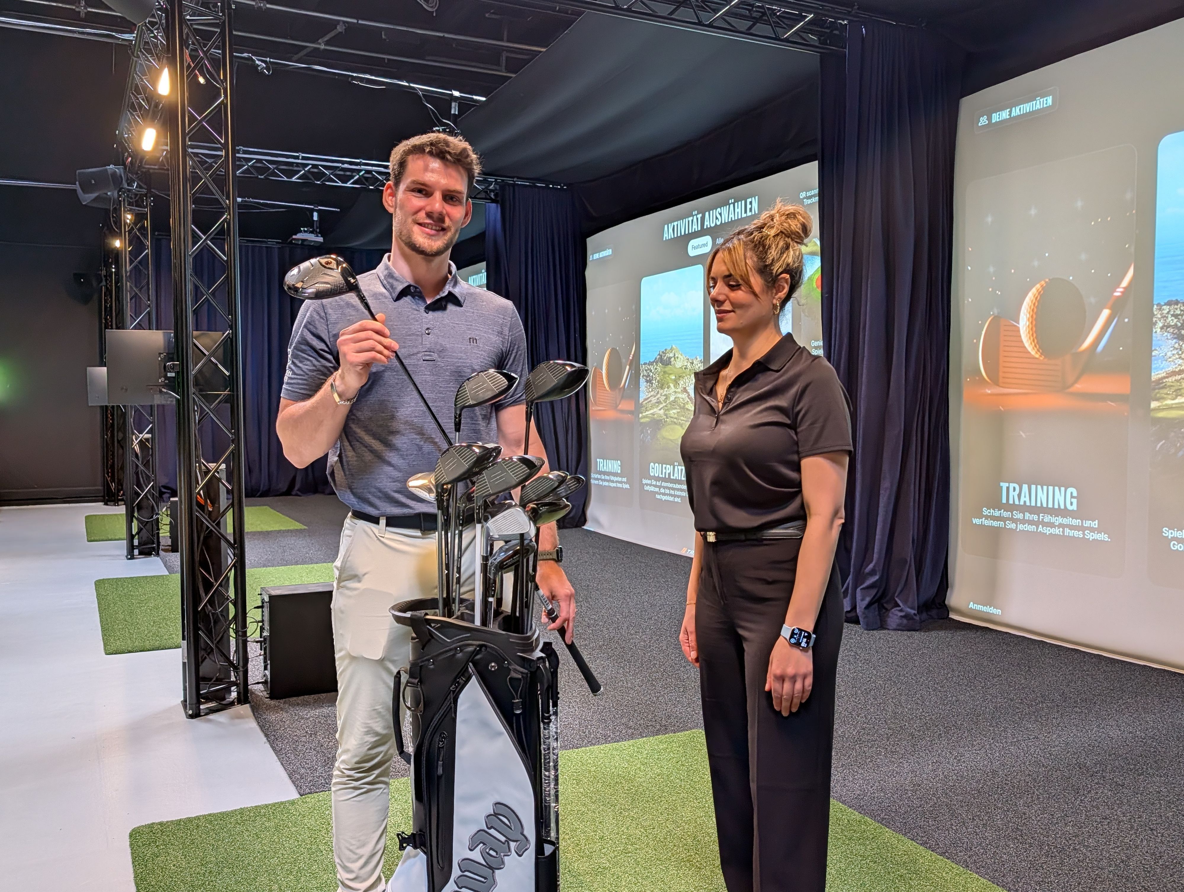 Das Foto zeigt das Inhaberpaar mit Golfausrüstung in der Golfhalle.