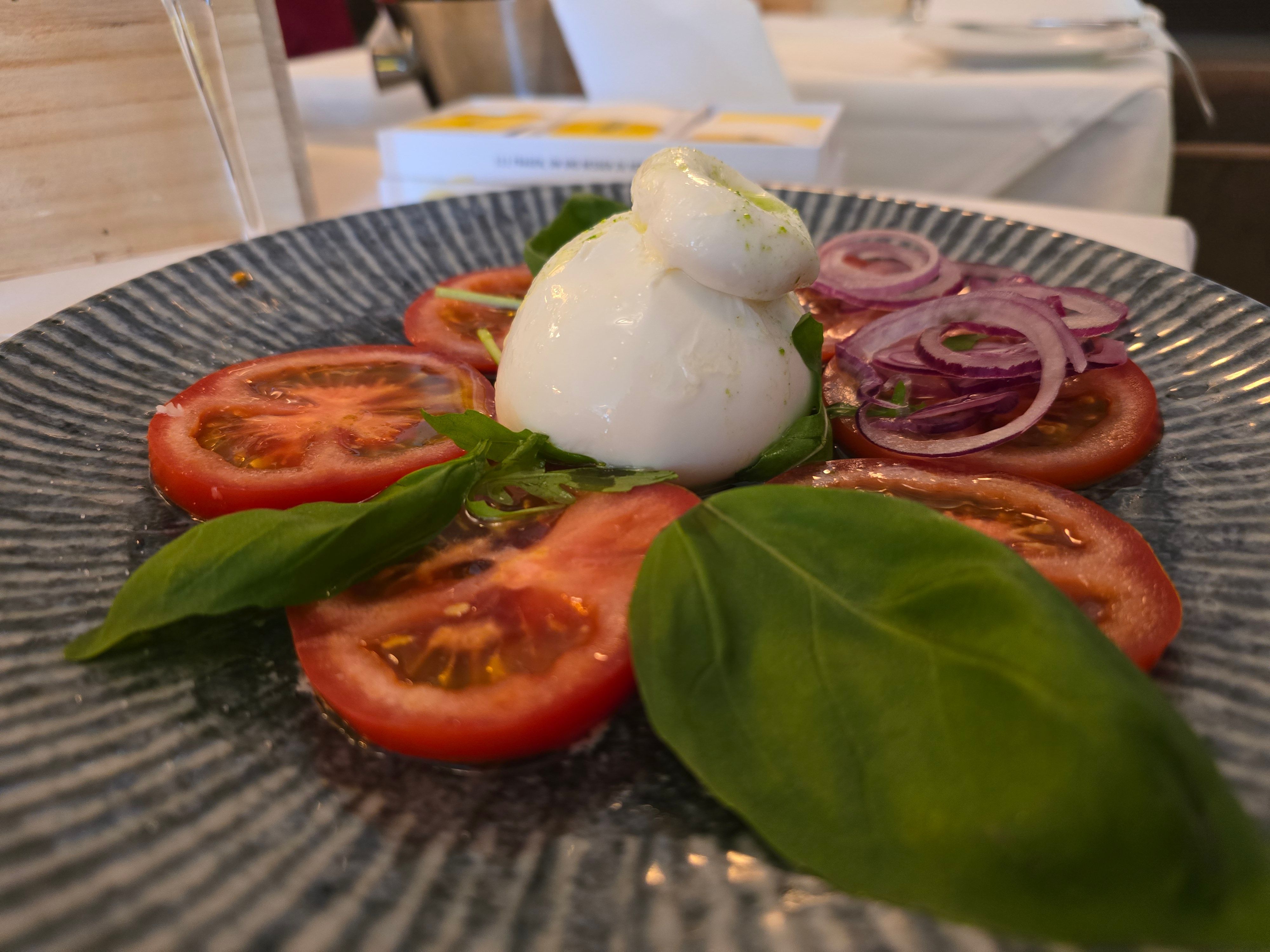 Tellergericht mit Tomatenscheiben, Burrata und Basilikum ist zu sehen