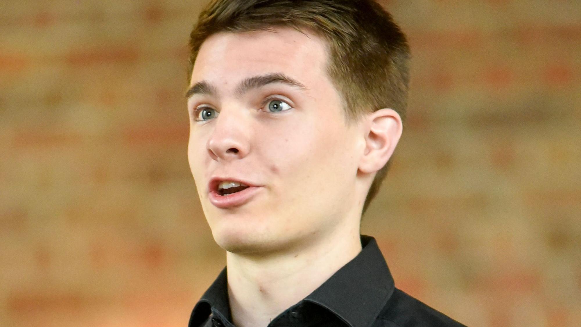 Auf dem Bild ist ein junger Mann zu sehen, der singt.